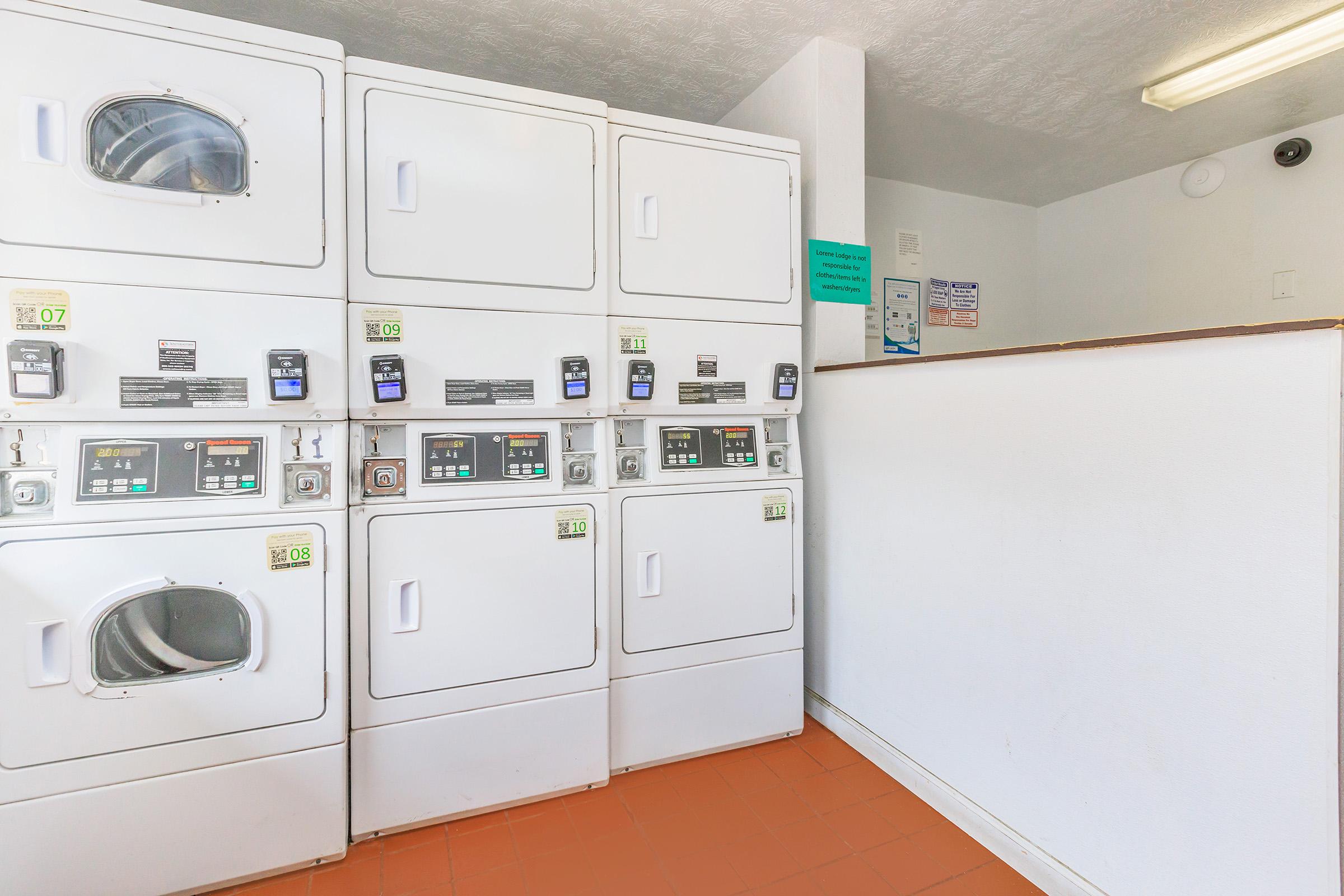 A clean and well-maintained laundromat interior featuring several stacked washing machines and dryers. The machines are equipped with digital screens and coin slots, and a service counter is visible in the background. Bright lighting enhances the space, creating an inviting atmosphere for laundry tasks.