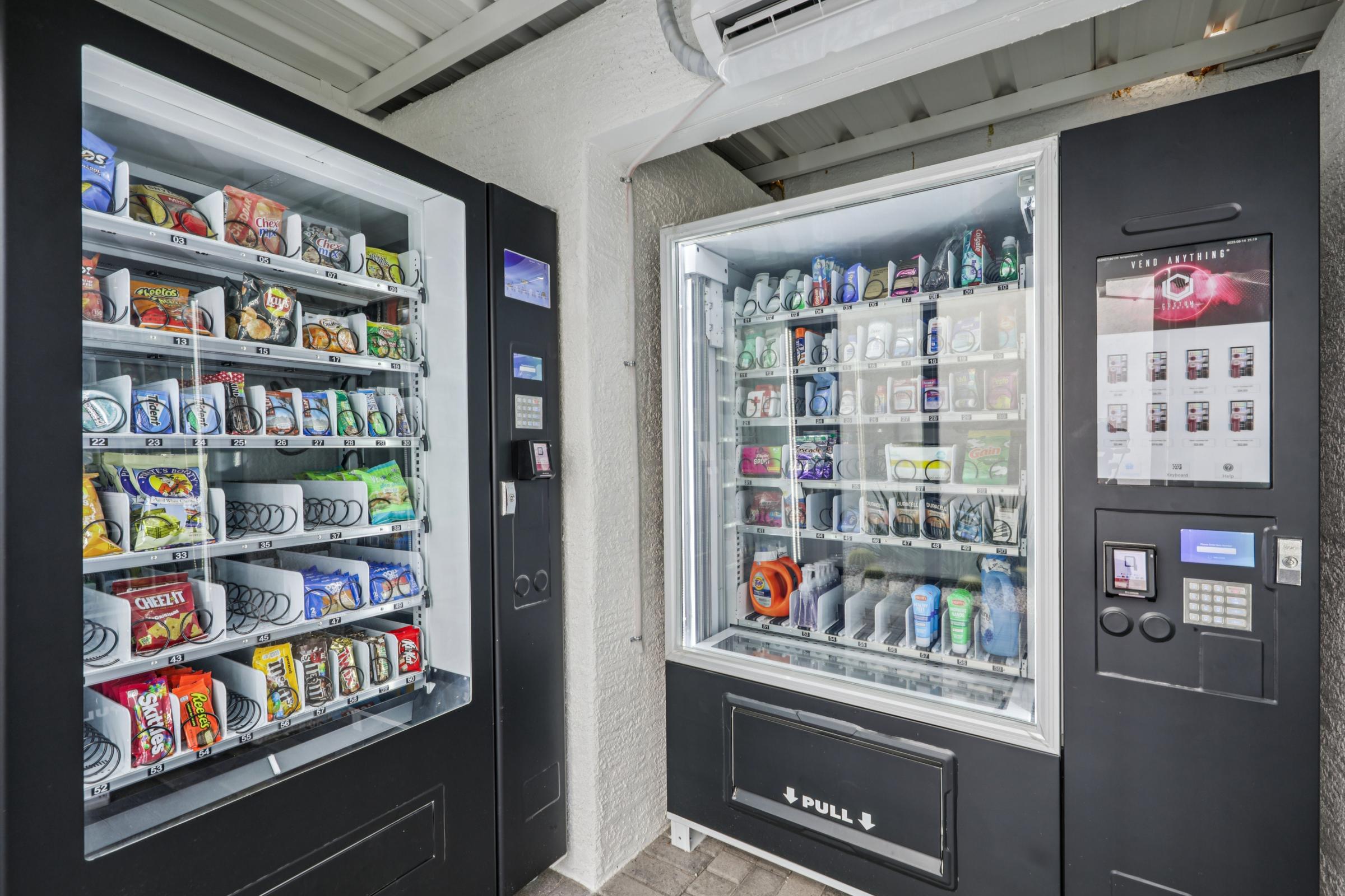 Two vending machines located in a well-lit area. The left machine dispenses various snacks like chips and candy, while the right one offers drinks, including cans and bottles. Both machines have digital displays and payment options. The setting is clean and modern.