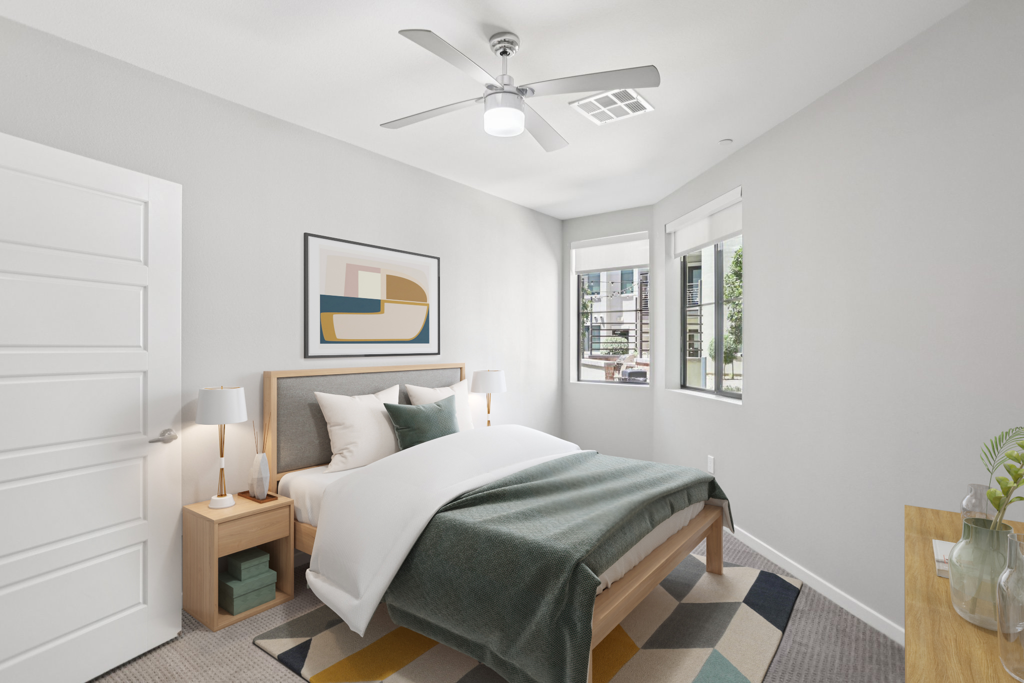 A modern bedroom featuring a wooden bed with white bedding and a dark green throw. Two bedside lamps are on either side of the bed. There is a colorful rug on the floor and a small table with plants. Large windows let in natural light, highlighting the neutral gray walls and minimalist decor.