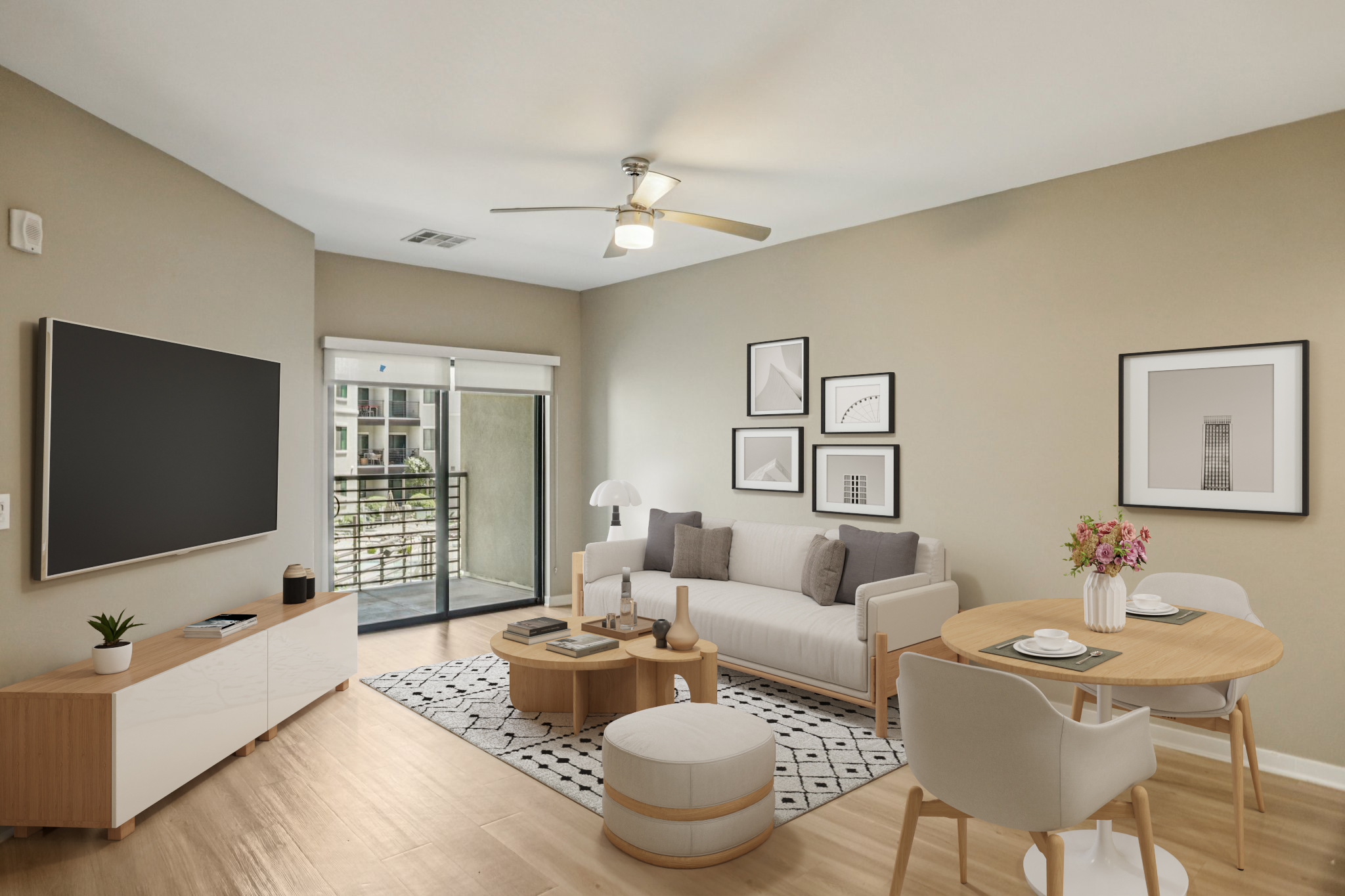 A modern living room featuring a light-colored sofa, a round coffee table, and a dining area with a small round table and chairs. Large windows allow natural light, and artwork is displayed on the walls. A plant and decorative items are arranged on the coffee table, creating a cozy atmosphere.