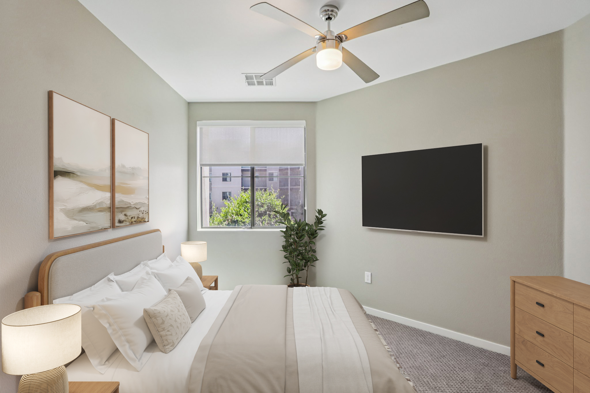 A modern bedroom featuring a queen-sized bed with white linens and decorative pillows, two bedside lamps, a wall-mounted flat-screen TV, a dresser, and a large window with greenery visible outside. Soft neutral tones and contemporary artwork enhance the cozy atmosphere.