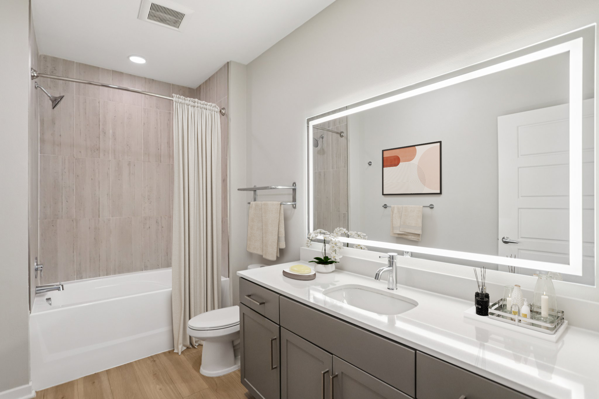 A modern bathroom featuring a bathtub with a shower curtain, a sleek vanity with a large mirror, a clean toilet, and minimalistic decor. The color palette is light and neutral, contributing to a bright and airy atmosphere. Accessories include towels and decorative items on the vanity.