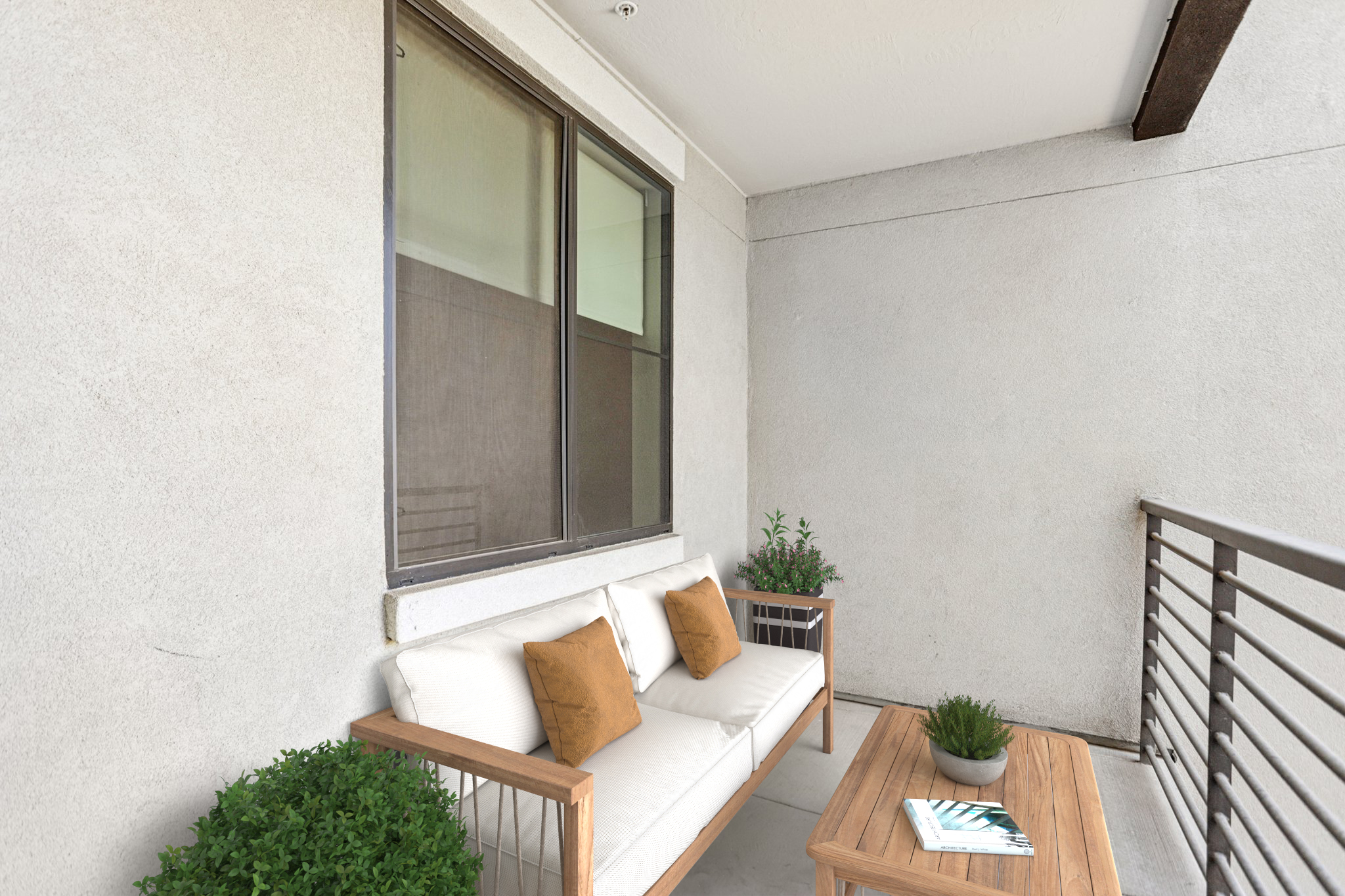 A cozy balcony featuring a modern outdoor sofa with plush cushions and decorative pillows, accompanied by a wooden coffee table. Two small green plants are positioned on either side of the sofa, and a railing is visible in the background, creating a serene and inviting space.
