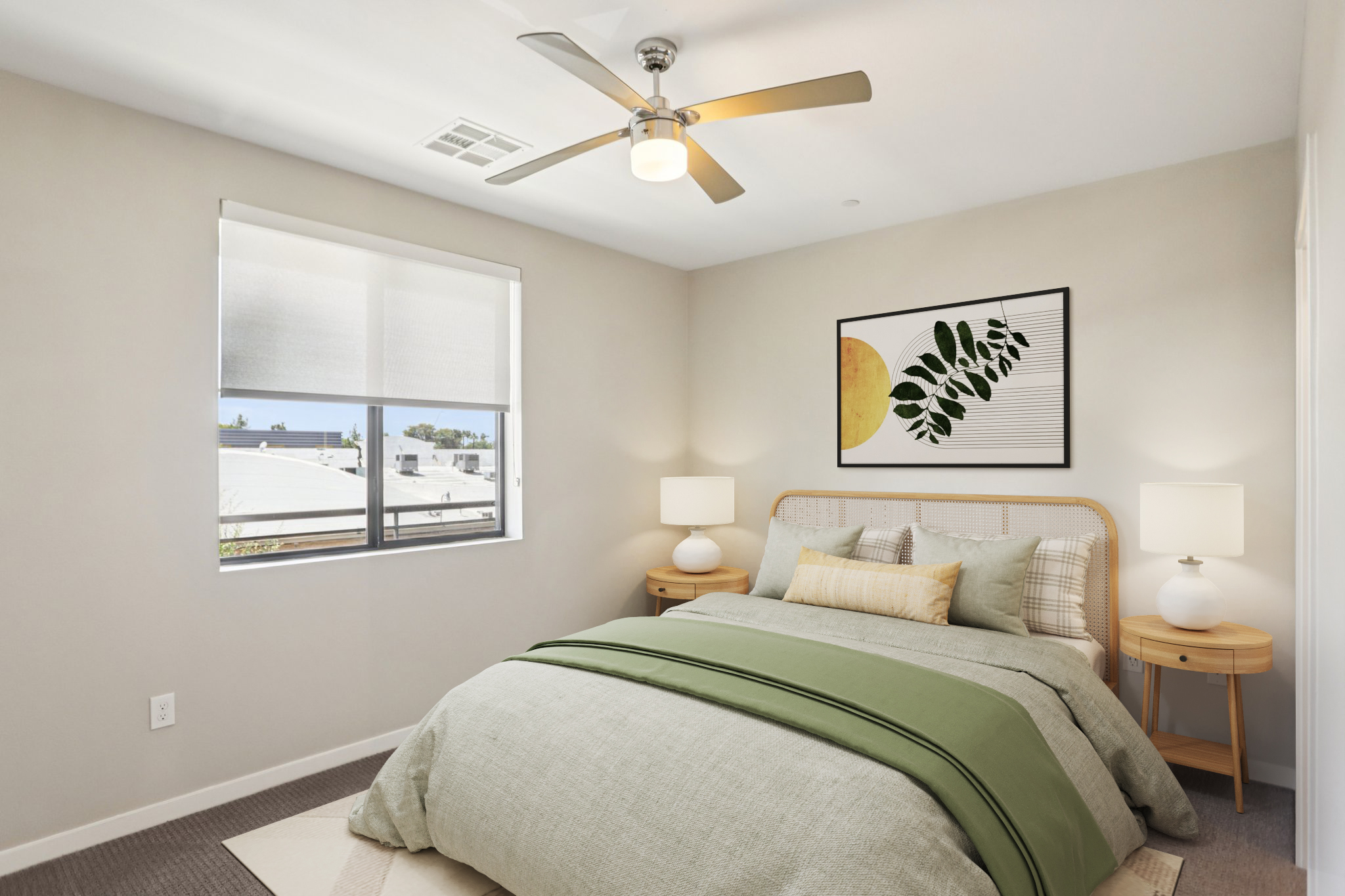 A cozy bedroom featuring a bed with a green and beige color scheme, two bedside tables with lamps, a modern ceiling fan, and a large window letting in natural light. A framed artwork with a leaf design and a yellow circle adorns the wall, adding a touch of style to the space.