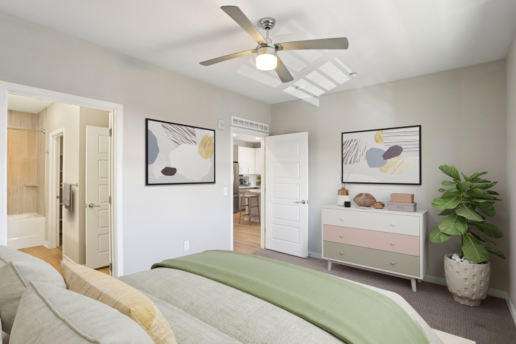 A stylish bedroom featuring a light gray color scheme, a bed with a green throw blanket, and decorative pillows. The walls are adorned with modern artwork. A doorway leads to a bathroom, and a potted plant is positioned next to a dresser with a mix of pastel colors. A ceiling fan adds to the airy ambiance.