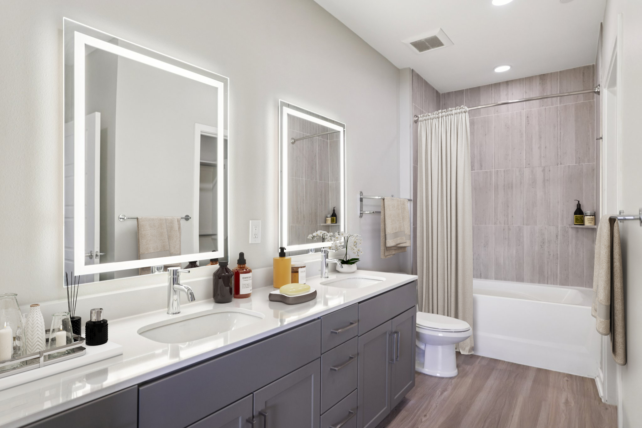 Modern bathroom featuring dual vanity sinks with backlit mirrors, a bathtub with a shower curtain, light gray walls, and wood-style flooring. Decorated with toiletries on the countertop and a small plant for a fresh look. Soft lighting enhances the clean and open feel of the space.