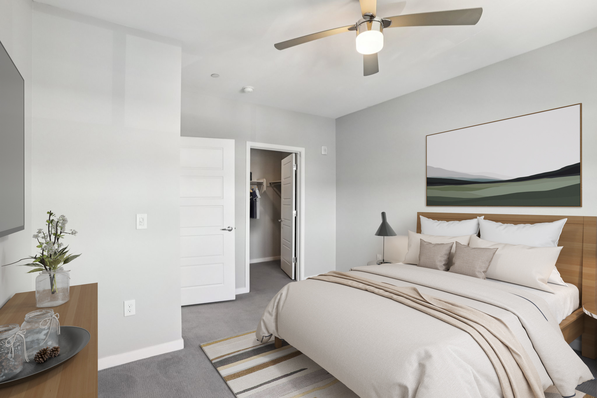 A modern bedroom featuring a neatly made bed with neutral-toned bedding, a stylish lamp on a side table, and a wall-mounted TV. A closet door is ajar, revealing clothes inside. The room has light gray walls and a large artwork above the bed depicting a serene landscape. A ceiling fan is visible, providing a cozy atmosphere.