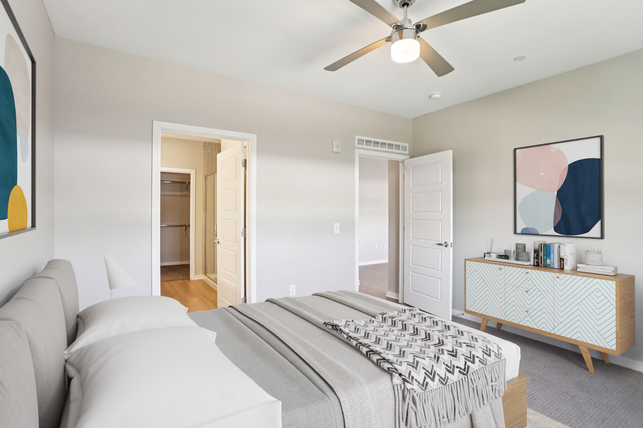 A modern bedroom featuring a gray bed with white pillows, a cozy blanket, and a stylish wooden dresser. The room has light-colored walls, a ceiling fan, and a large window. An open closet can be seen through the doorway, and there are decorative wall art pieces adding a contemporary touch.