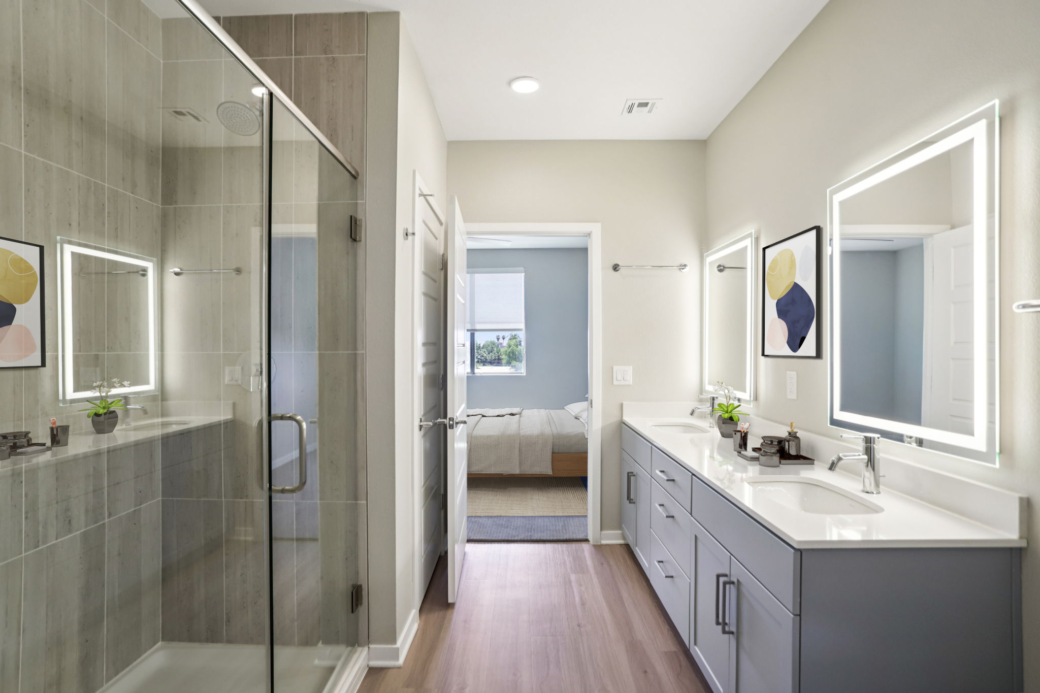 Modern bathroom featuring a glass shower with a tiled wall, dual sinks with illuminated mirrors, and minimalist decor. There are light gray cabinets, small potted plants on the counter, and a glimpse of a bedroom through an open door in the background. Natural light brightens the space.