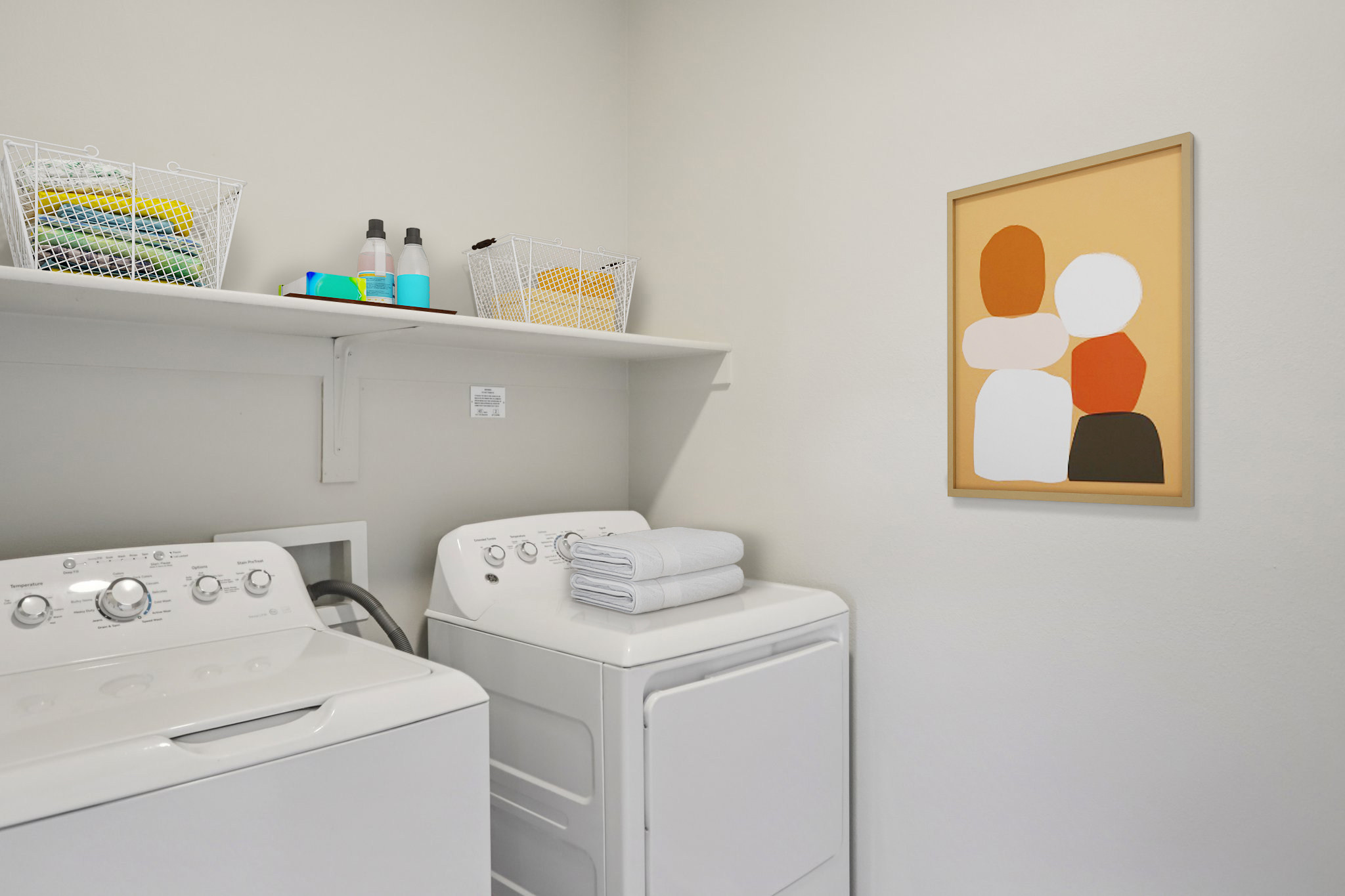 A laundry room featuring a washing machine and dryer, stacked with neatly folded towels and detergent bottles. Above, a shelf holds colorful laundry baskets. A modern art piece with abstract shapes in earthy tones is displayed on the wall, adding a touch of style to the space.