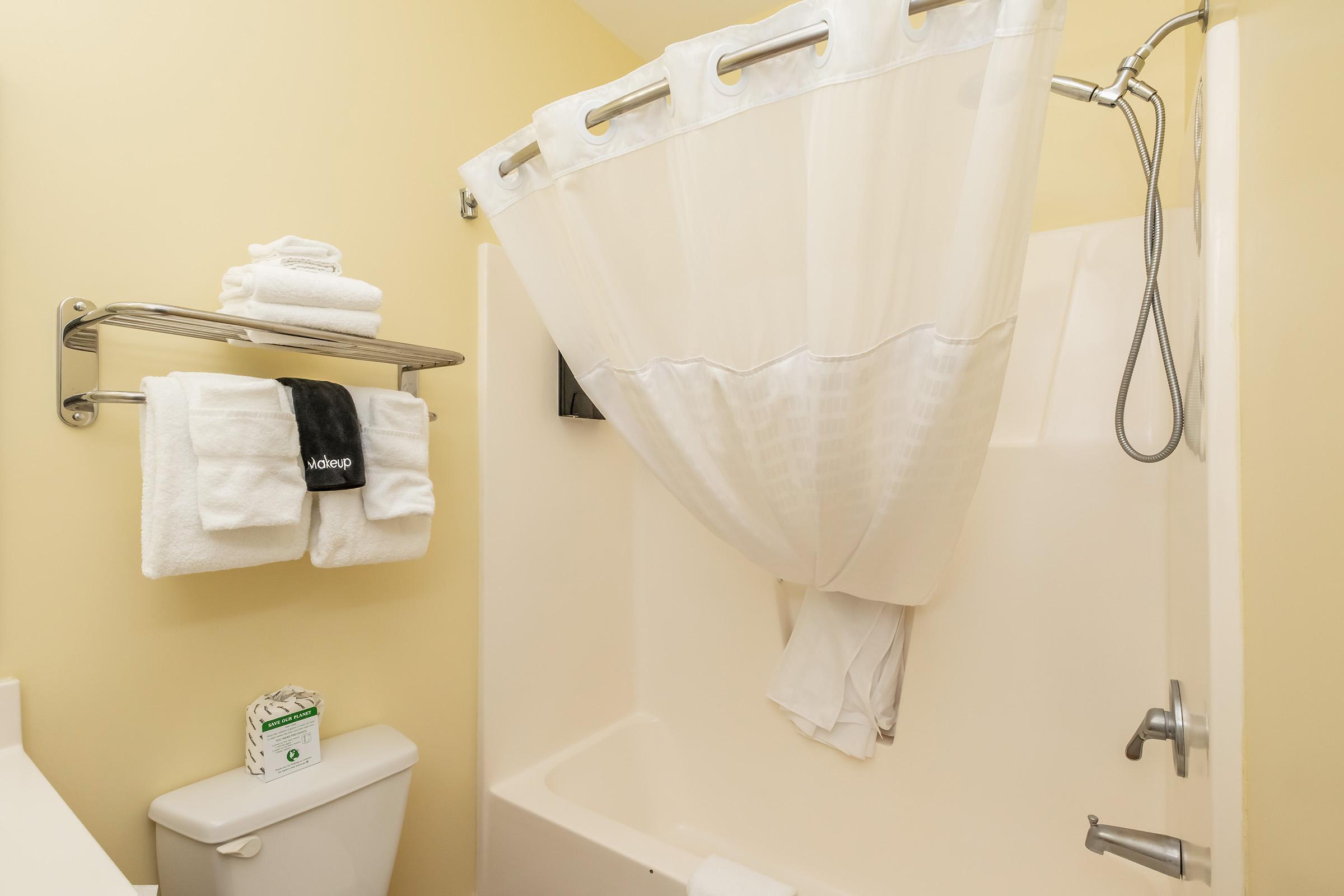 A clean bathroom featuring a bathtub with a shower curtain, neatly arranged white towels on a rack, and toiletries on the counter. The walls are painted in a light yellow hue, creating a bright and inviting atmosphere.