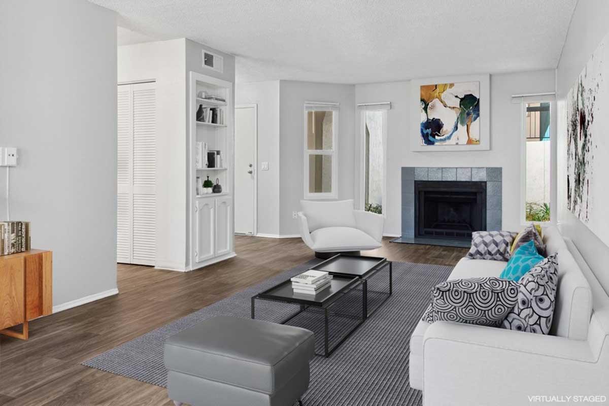 Modern living room featuring light gray walls and hardwood flooring. A white couch with colorful throw pillows is positioned opposite a sleek black coffee table. There’s a gray area rug, a stylish armchair, and an elegant fireplace. Large windows allow natural light, with abstract artwork on the wall.