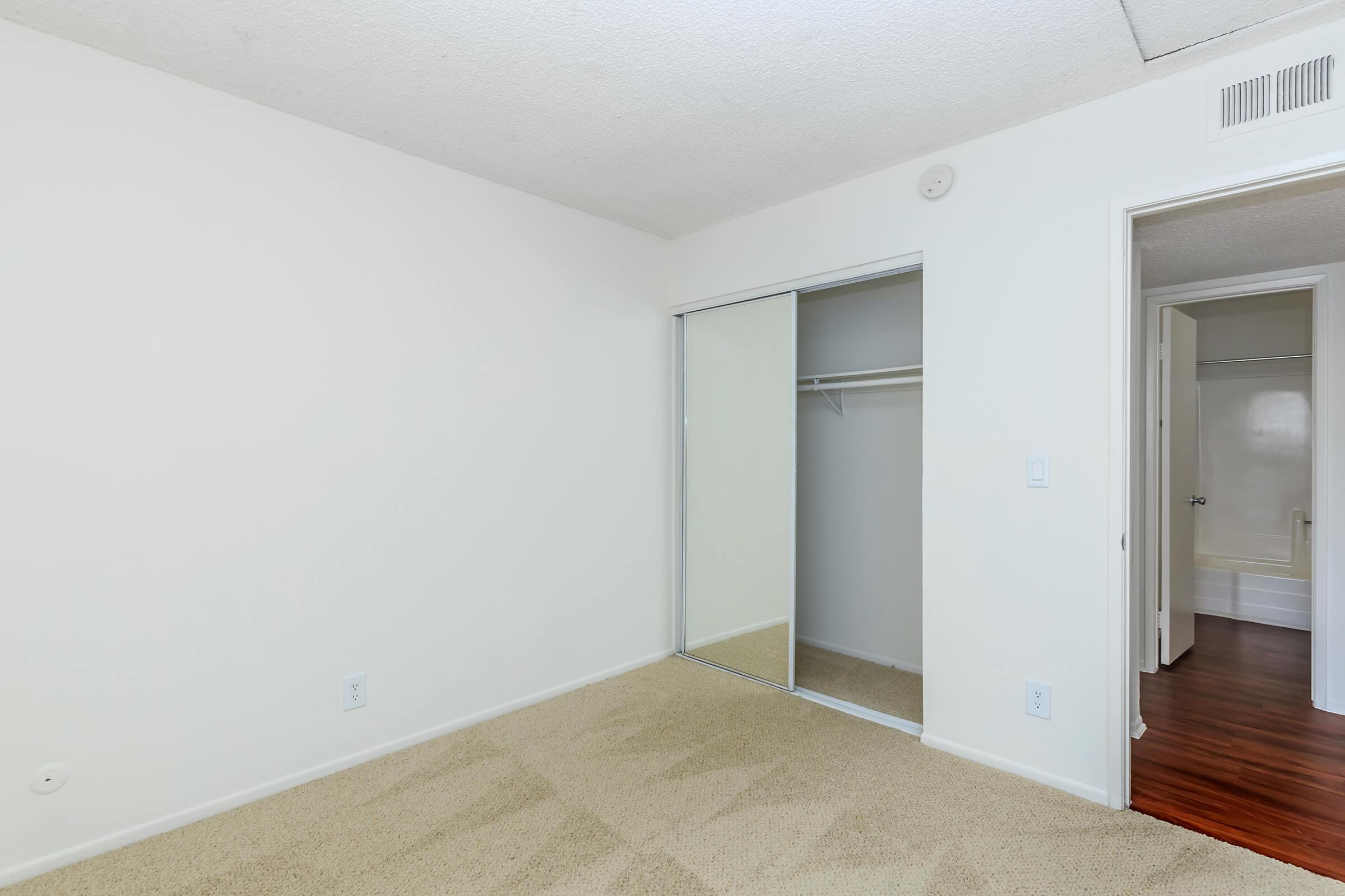 Carpeted bedroom with open sliding mirror glass closet door