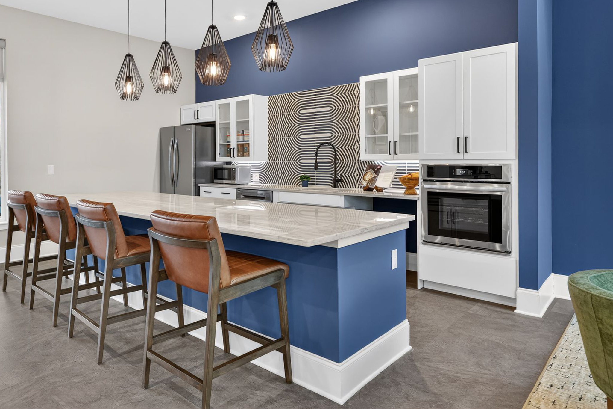 Modern kitchen featuring a navy blue accent wall, white cabinetry, and stainless steel appliances. A large island with a light-colored countertop and bar stools provides seating. Pendant lights hang above the island, adding stylish illumination to the space.