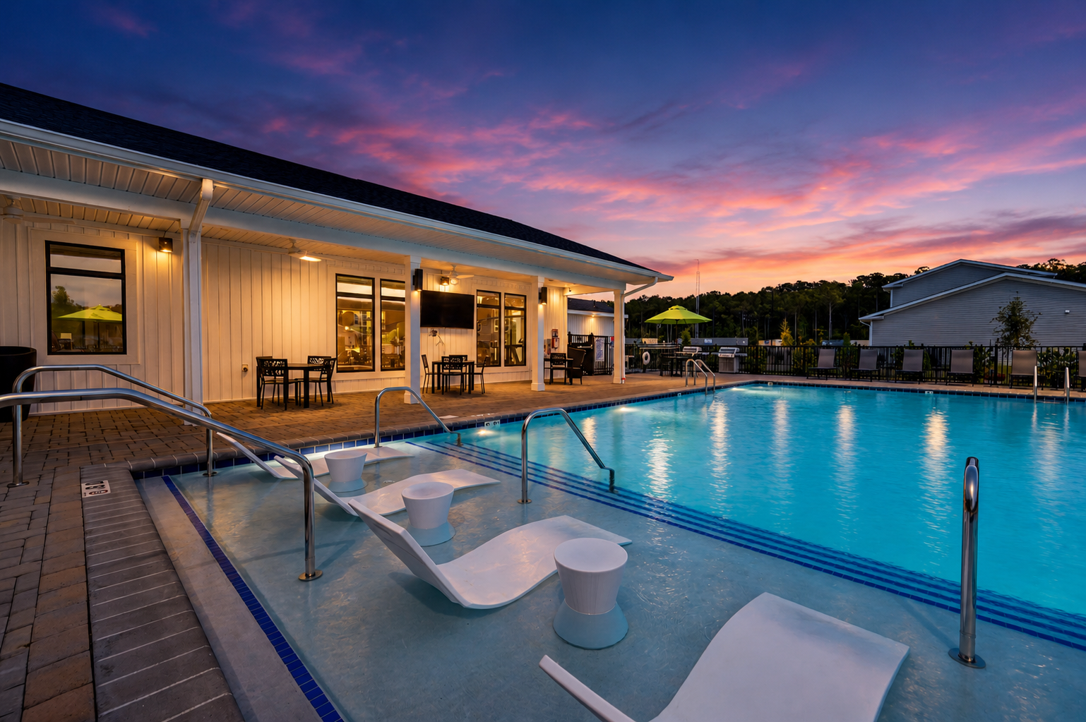 A serene evening scene featuring a swimming pool with clear blue water, surrounded by lounge chairs and tables. The sky is painted in vibrant hues of purple and pink as the sun sets. In the background, a modern building with large windows complements the tranquil atmosphere.