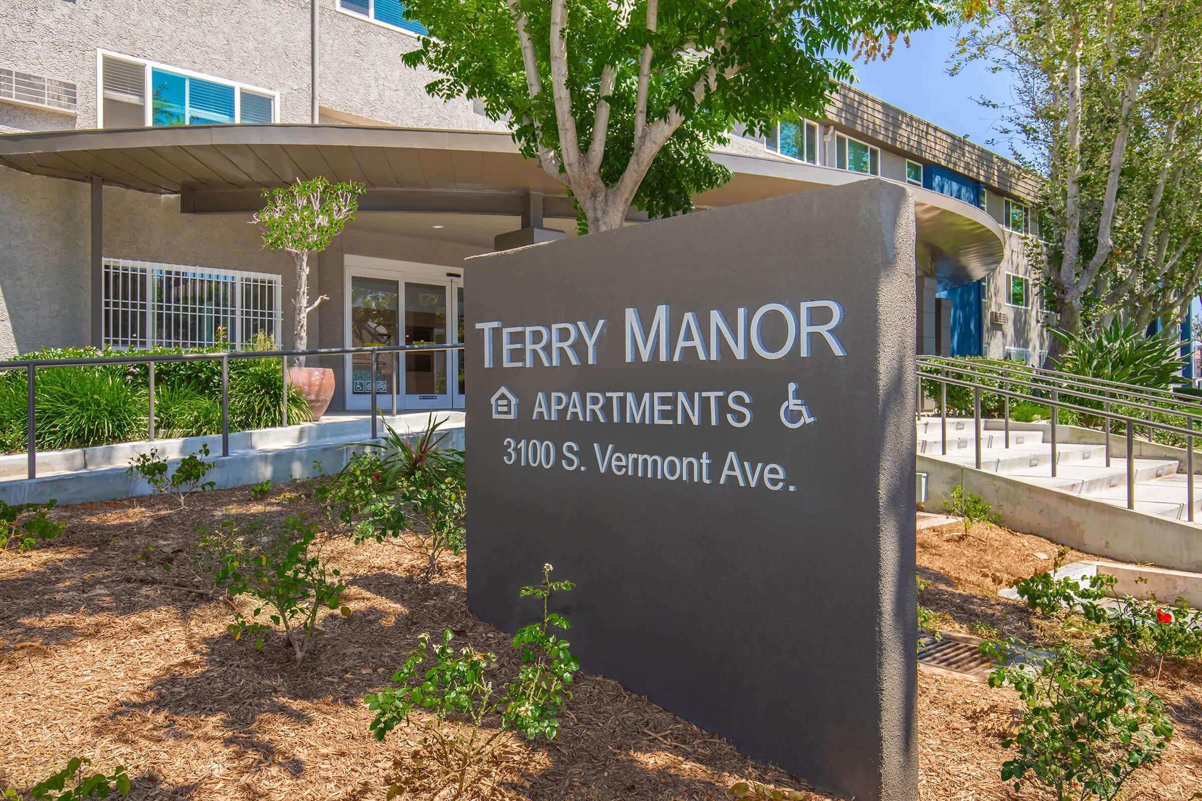 Sign for Terry Manor Apartments located at 3100 S. Vermont Ave, featuring greenery and accessible entrance. The building showcases a modern design with large windows.