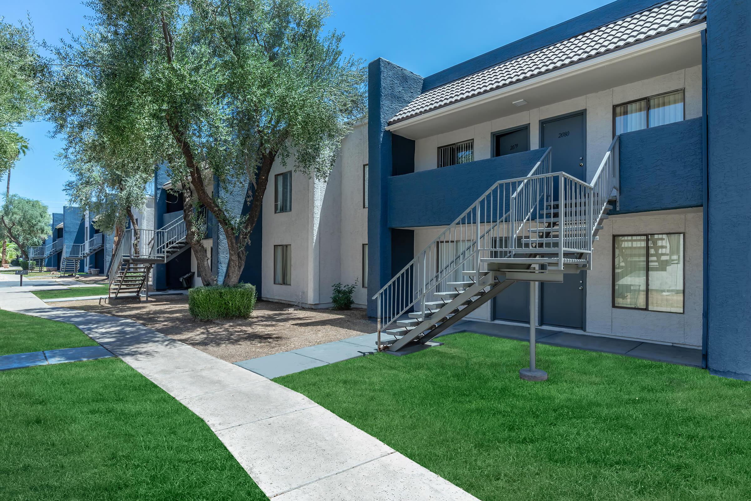 Blue and grey exterior apartment building tucked behind grass and sidewalk walkway