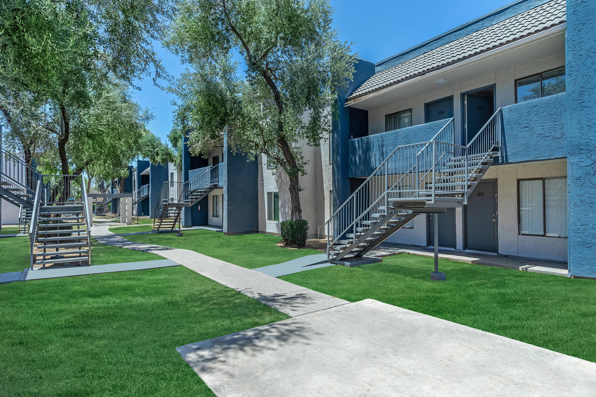 Blue and grey exterior Glendale apartment buildings around grass and sidewalk walkway