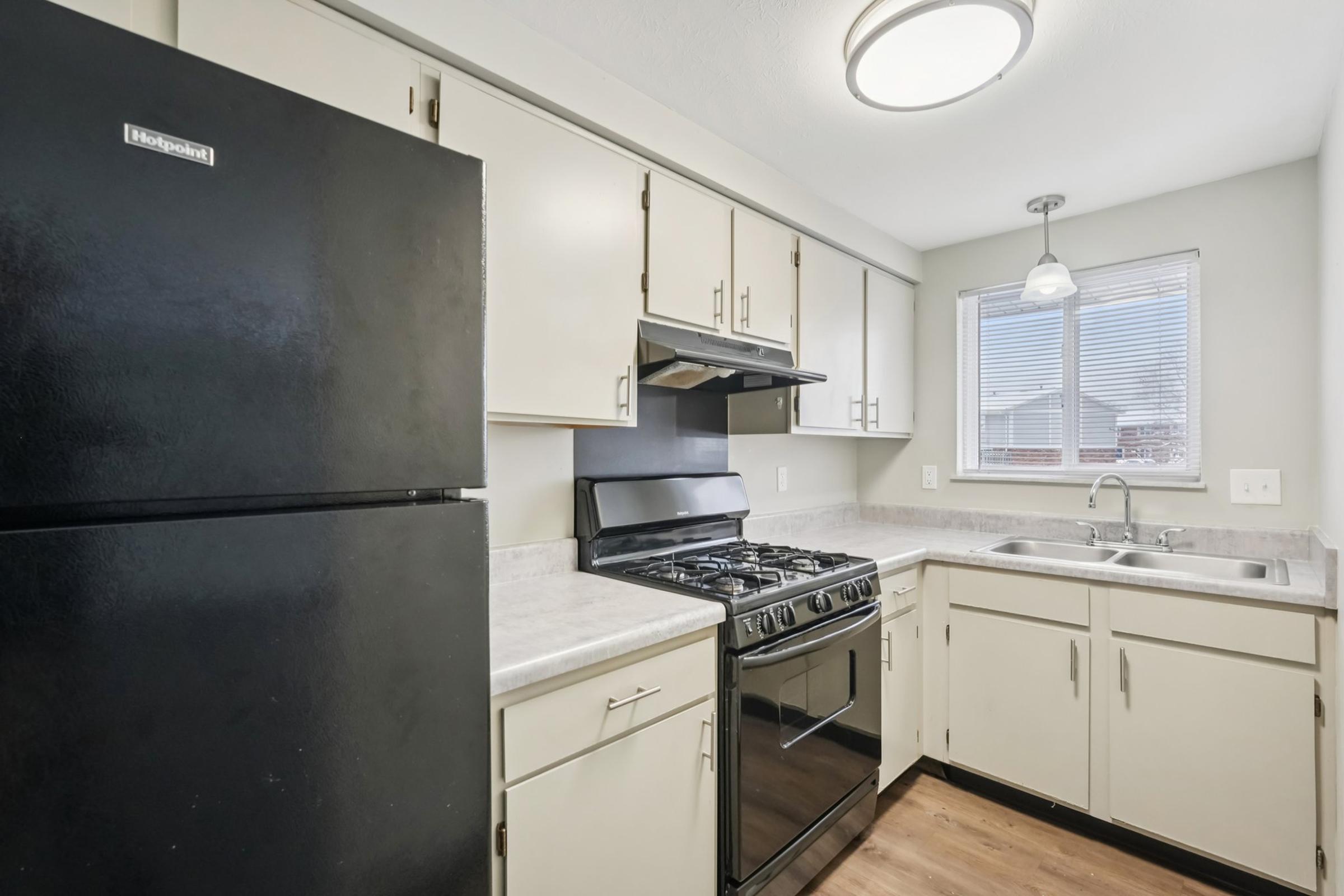 Modern kitchen featuring a black refrigerator, a stainless steel gas stove, and dual sinks. Light-colored cabinets complement the countertops. Natural light fills the space through a window, creating a bright and inviting atmosphere.