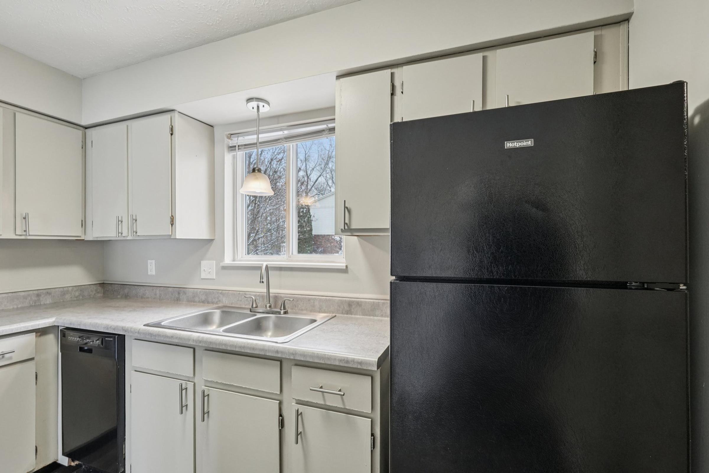 A clean, modern kitchen featuring light gray cabinets, a black refrigerator, a stainless steel dishwasher, and a double sink. Natural light comes in through a window above the sink, illuminating the countertop and creating a bright, inviting atmosphere.