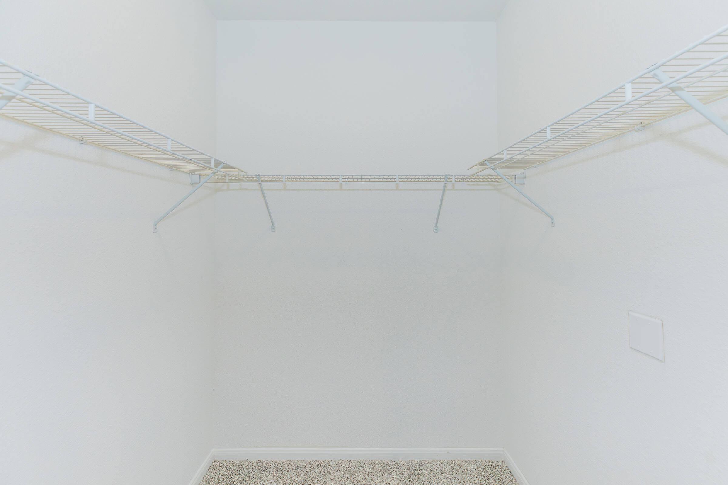 Empty closet with white walls and two wire shelving units installed on opposite sides, providing storage space. The floor is covered with a light-colored carpet, contributing to the minimalistic look of the space.