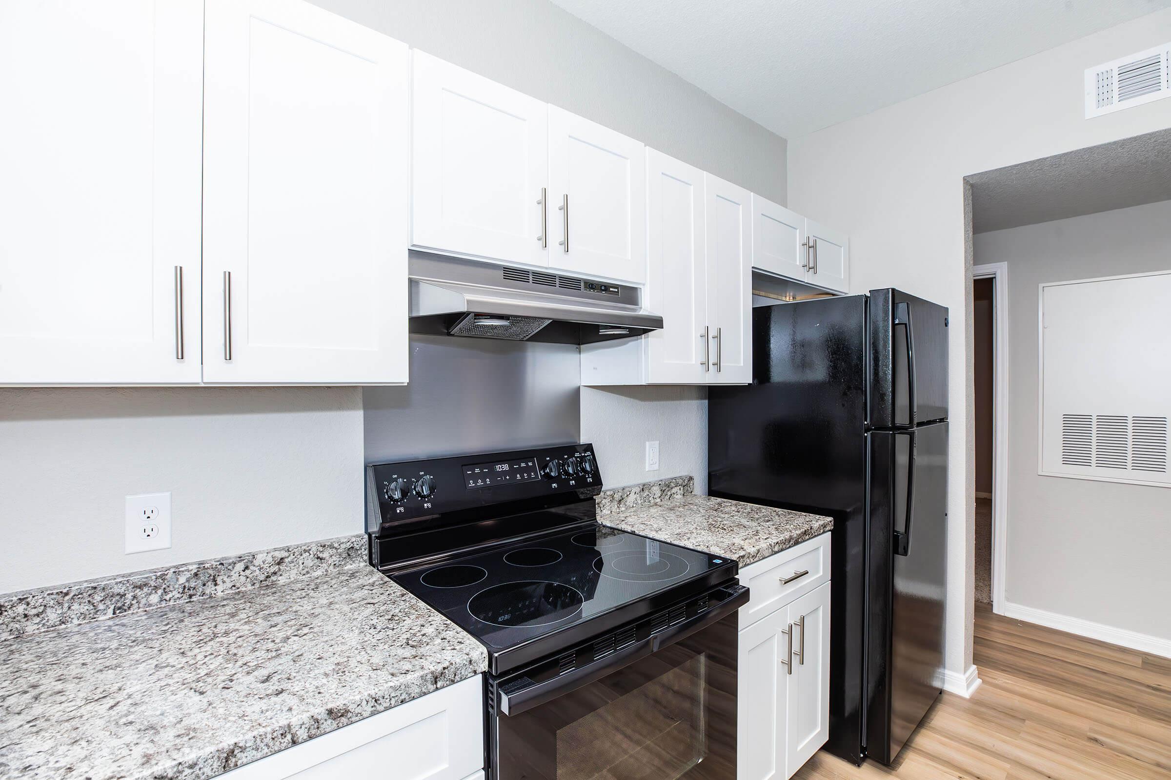 Modern kitchen featuring white cabinetry, granite countertops, a black stove and microwave, and a black refrigerator. The space has light wood flooring and neutral-colored walls, creating a bright and inviting atmosphere.