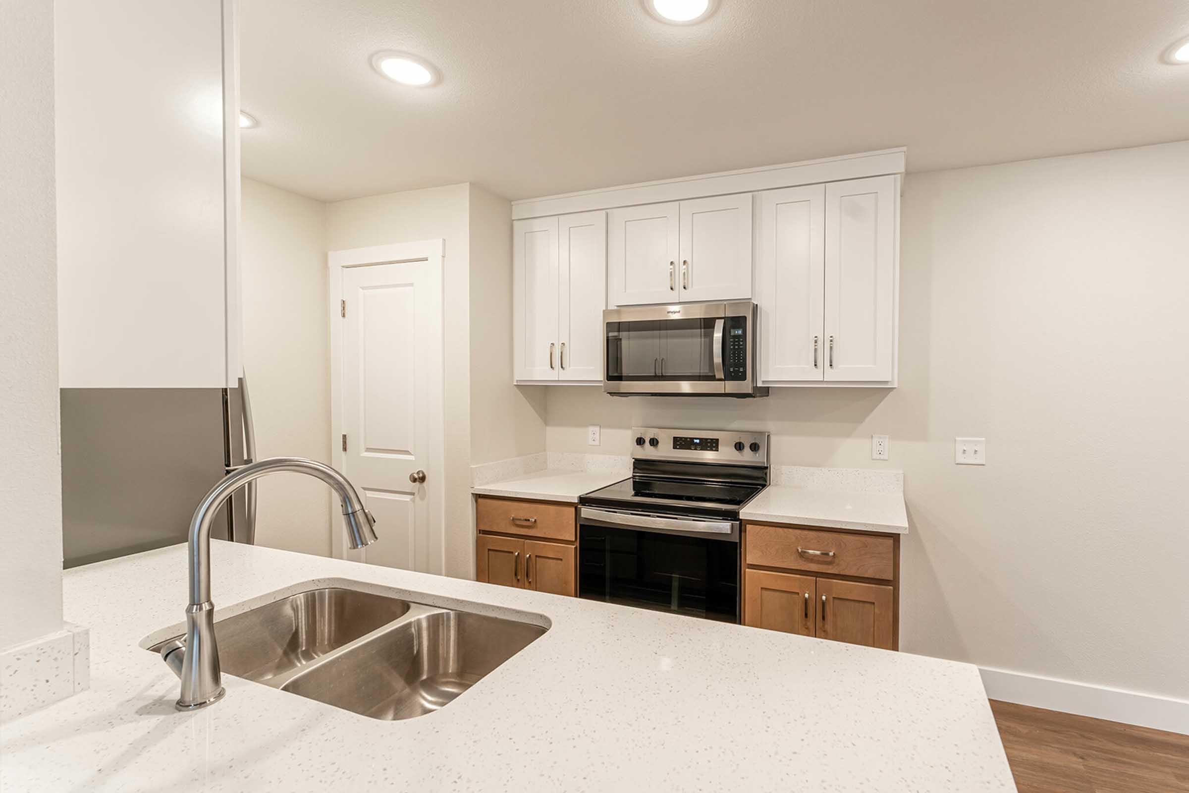 Modern kitchen with white cabinetry and stainless steel appliances. Features include a microwave above a stove, a double sink, and quartz countertops. Light fixtures provide bright illumination, and the walls are painted in neutral tones, creating a clean and contemporary aesthetic.