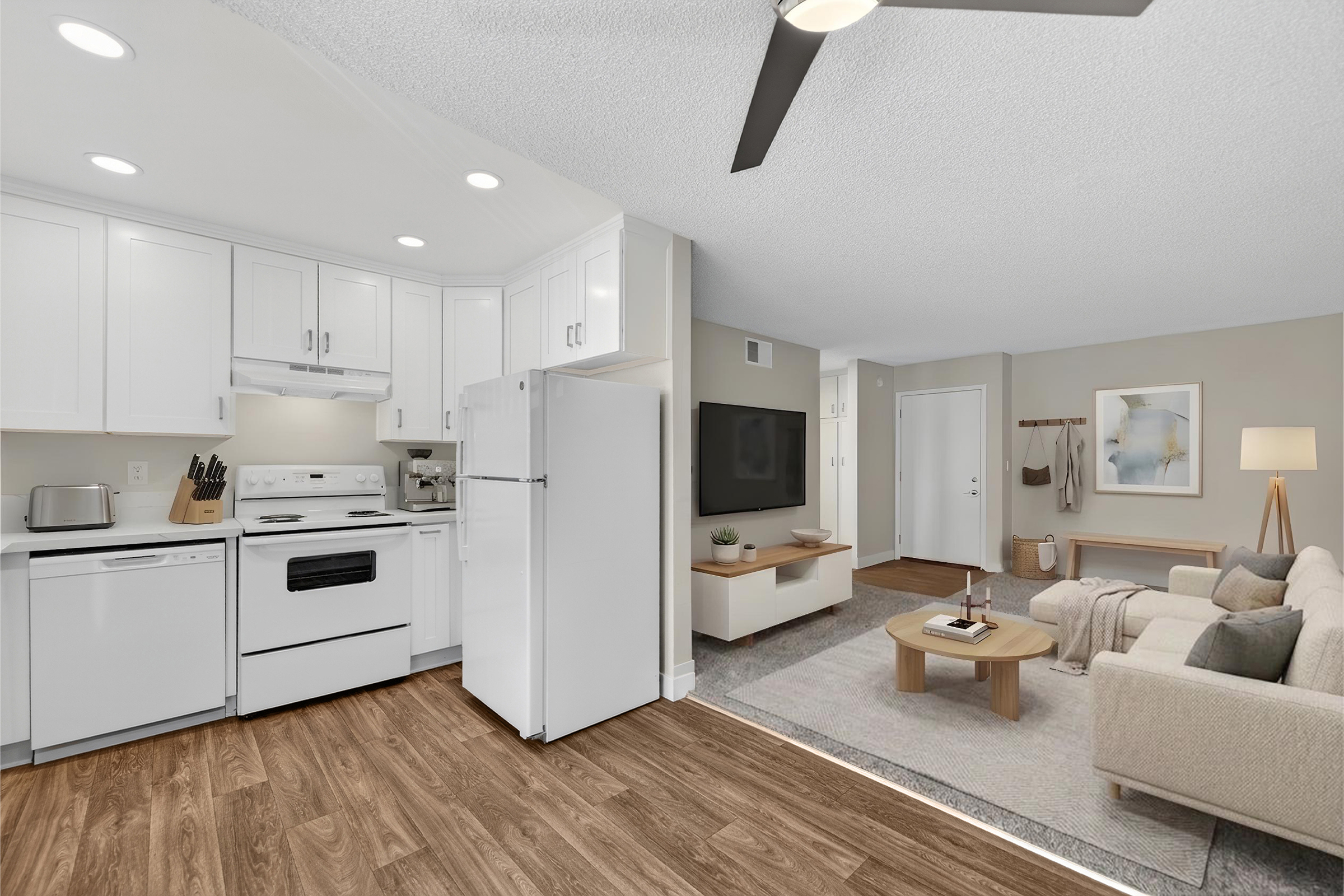 A modern living space featuring an open floor plan. On the left, a bright kitchen with white cabinets, a stove, and a refrigerator. On the right, a cozy living area with a light-colored sofa, a coffee table, and a TV mounted on the wall. The flooring is a warm brown wood, and the walls are painted in soft neutral tones.
