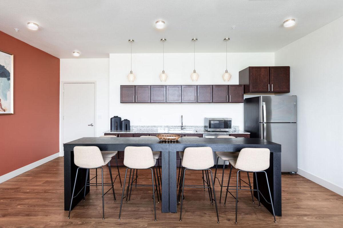 Modern kitchen featuring a large island with high stools, dark wood cabinetry, stainless steel appliances including a refrigerator, and a microwave.