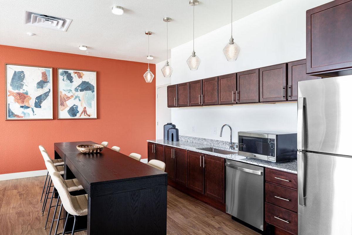 Modern kitchen featuring dark wood cabinets, a stainless-steel refrigerator, and a microwave. The countertop is made of granite, with decorative lighting above.