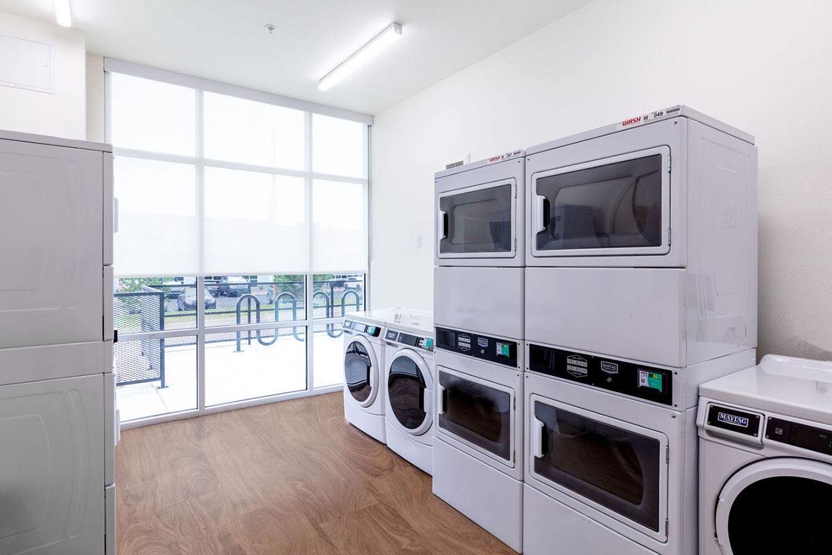 A bright laundry room featuring several stacked white washers and dryers against a light-colored wall