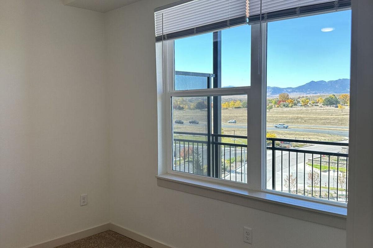 A bright, empty room with a large window showcasing a view of distant mountains and a clear blue sky.
