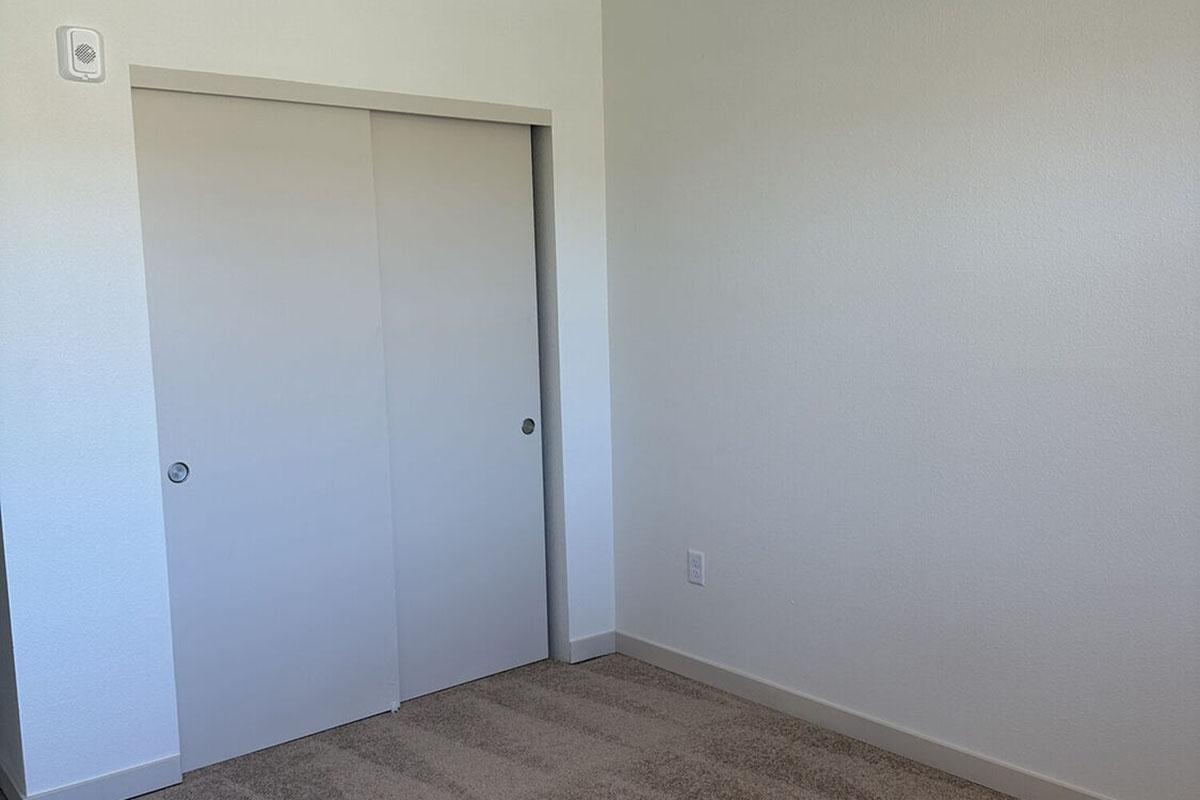 A simple, empty room with light-colored walls and beige carpet.