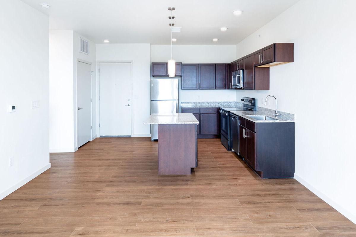 Modern kitchen featuring dark wooden cabinets, stainless steel appliances, a granite countertop island, and a light-colored wall.
