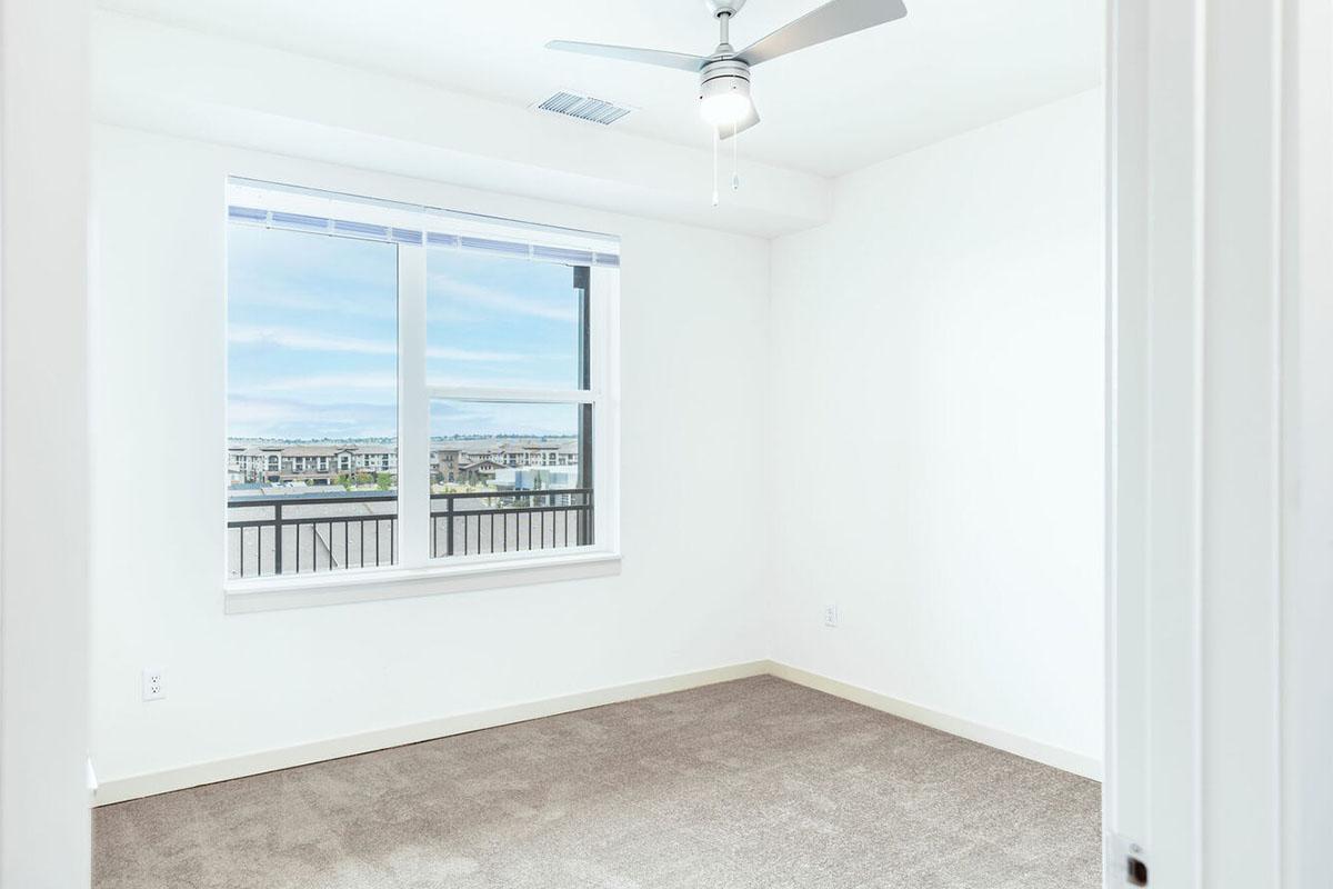 A modern, empty room with light-colored walls and a large window offering a view of the outdoors.