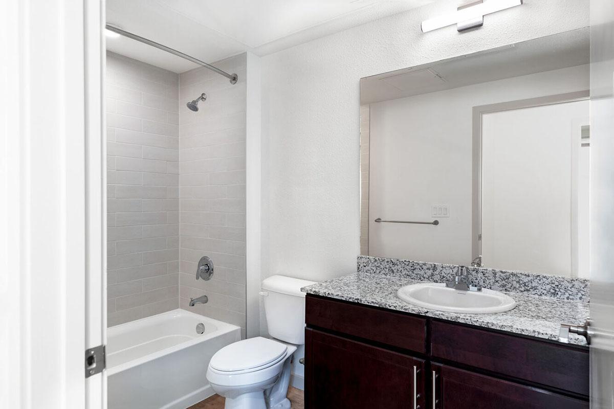 A modern bathroom featuring a white bathtub with a showerhead, a toilet, and a vanity with a dark wood finish.