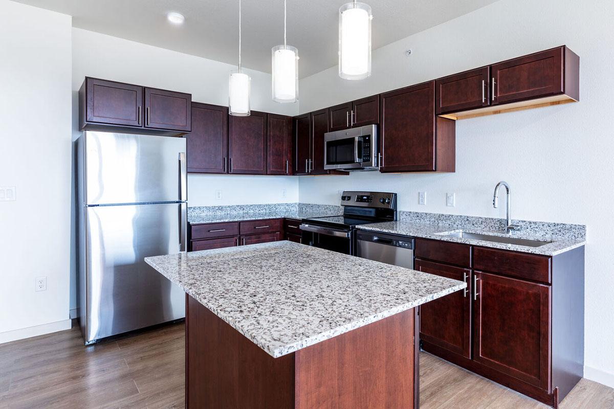 Modern kitchen featuring dark wood cabinetry, stainless steel appliances including a refrigerator and oven, and a center island with a granite countertop.