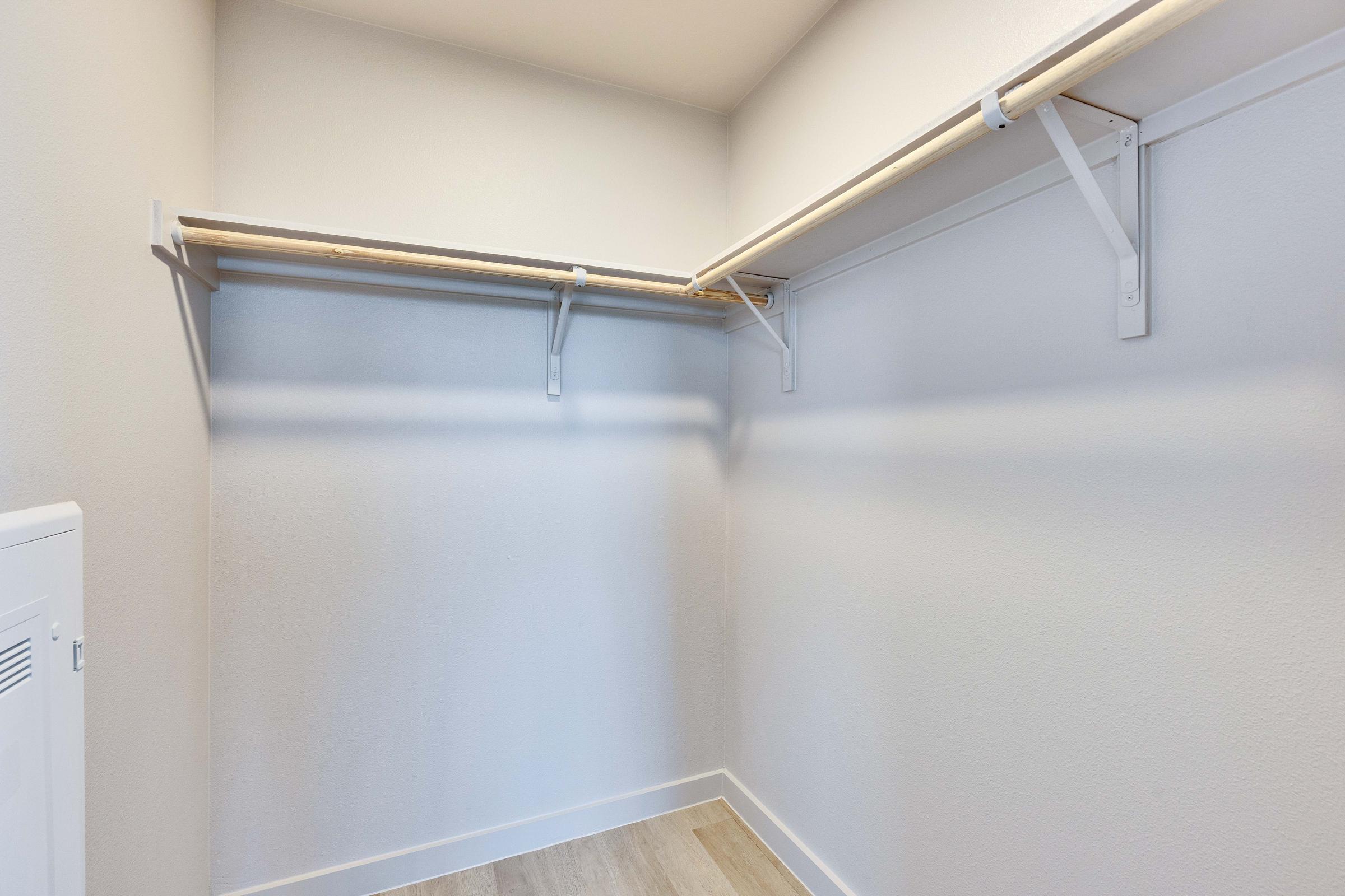 A spacious, empty closet featuring two wooden hanging rods mounted on the wall. The walls are painted a light color, and the floor has a wooden finish. The area is well-lit and clean, providing a blank canvas for organization and storage.