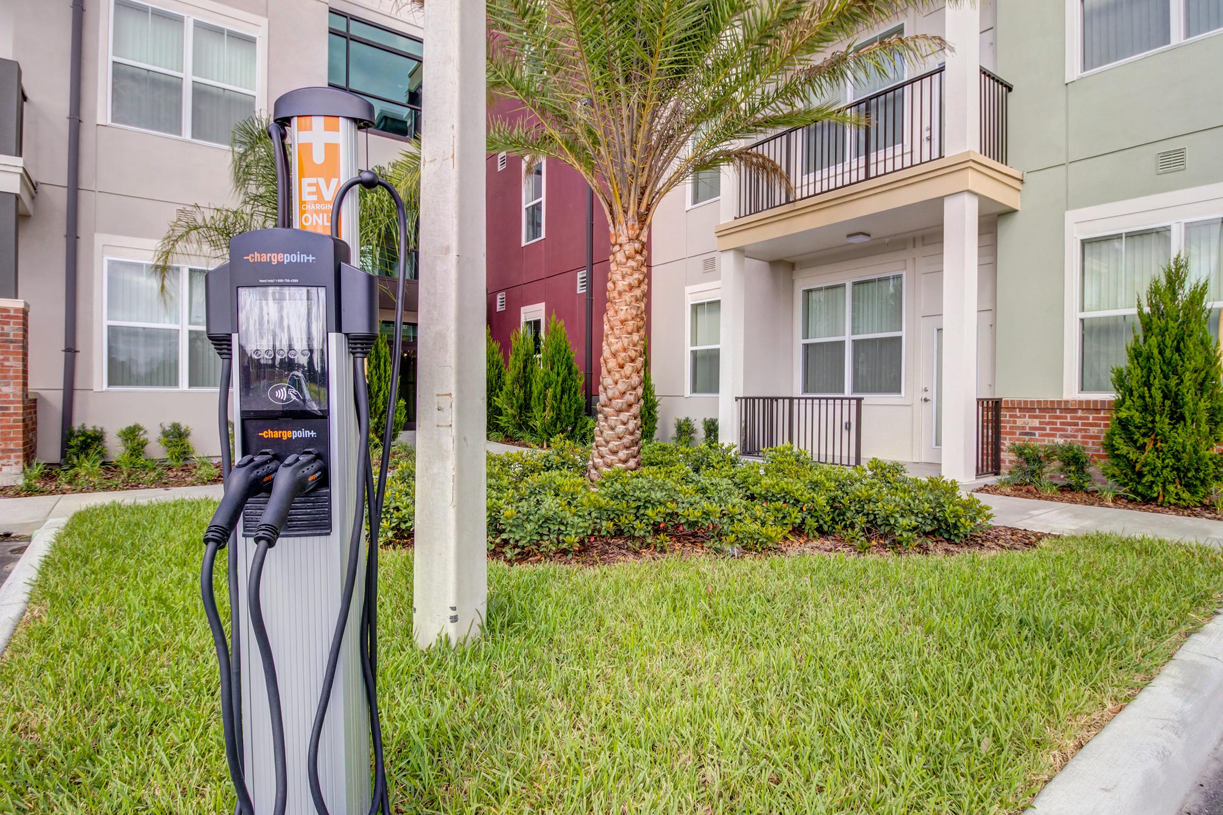 An electric vehicle charging station with multiple connectors is situated in front of a modern apartment building. The area features well-maintained landscaping, including palm trees and neatly trimmed grass, enhancing the residential environment.