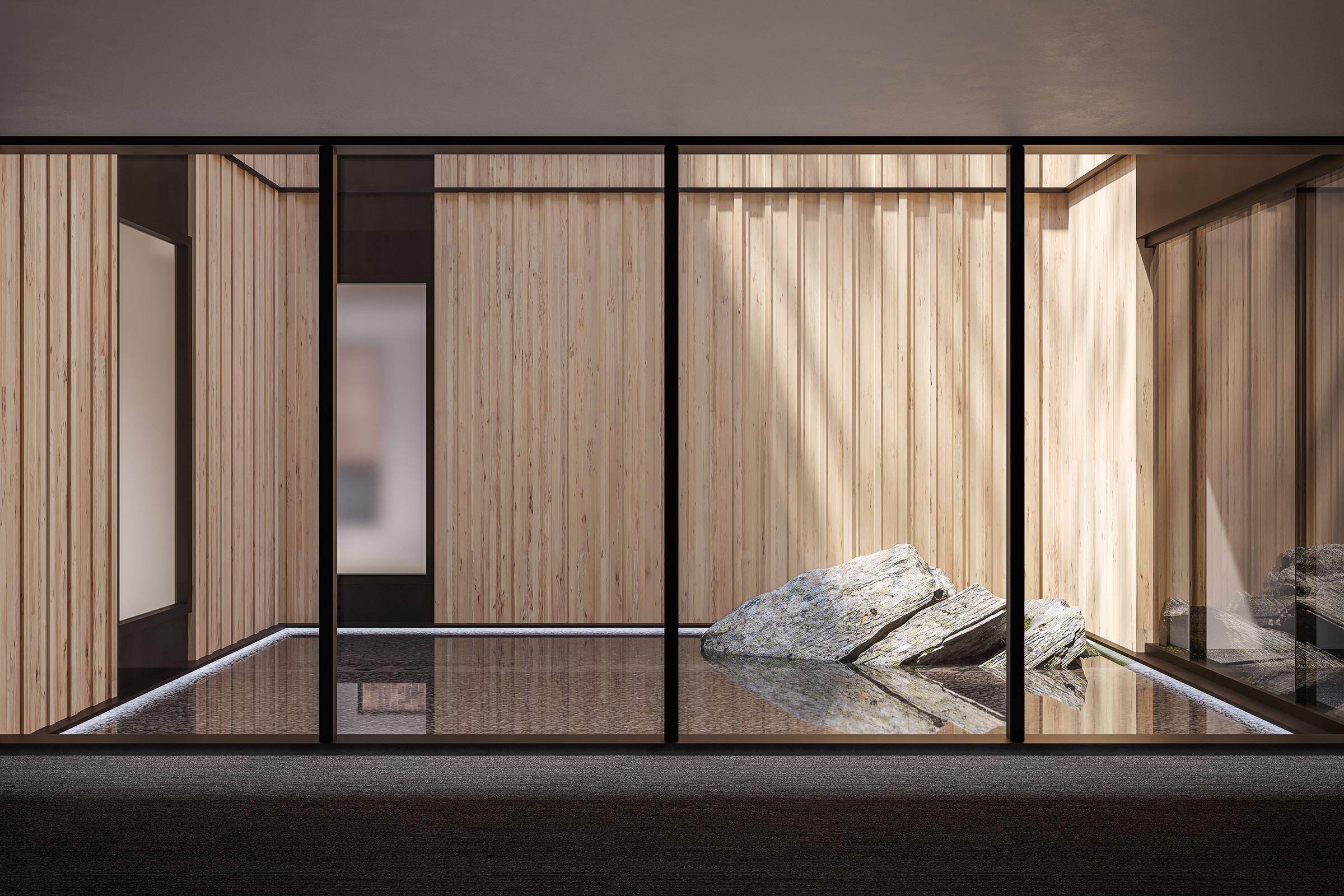 Interior view of a contemporary space featuring large glass panels. The walls are wooden, creating a warm atmosphere, while a natural stone formation is positioned on a reflective surface. Soft light filters in, enhancing the calming, minimalist design.