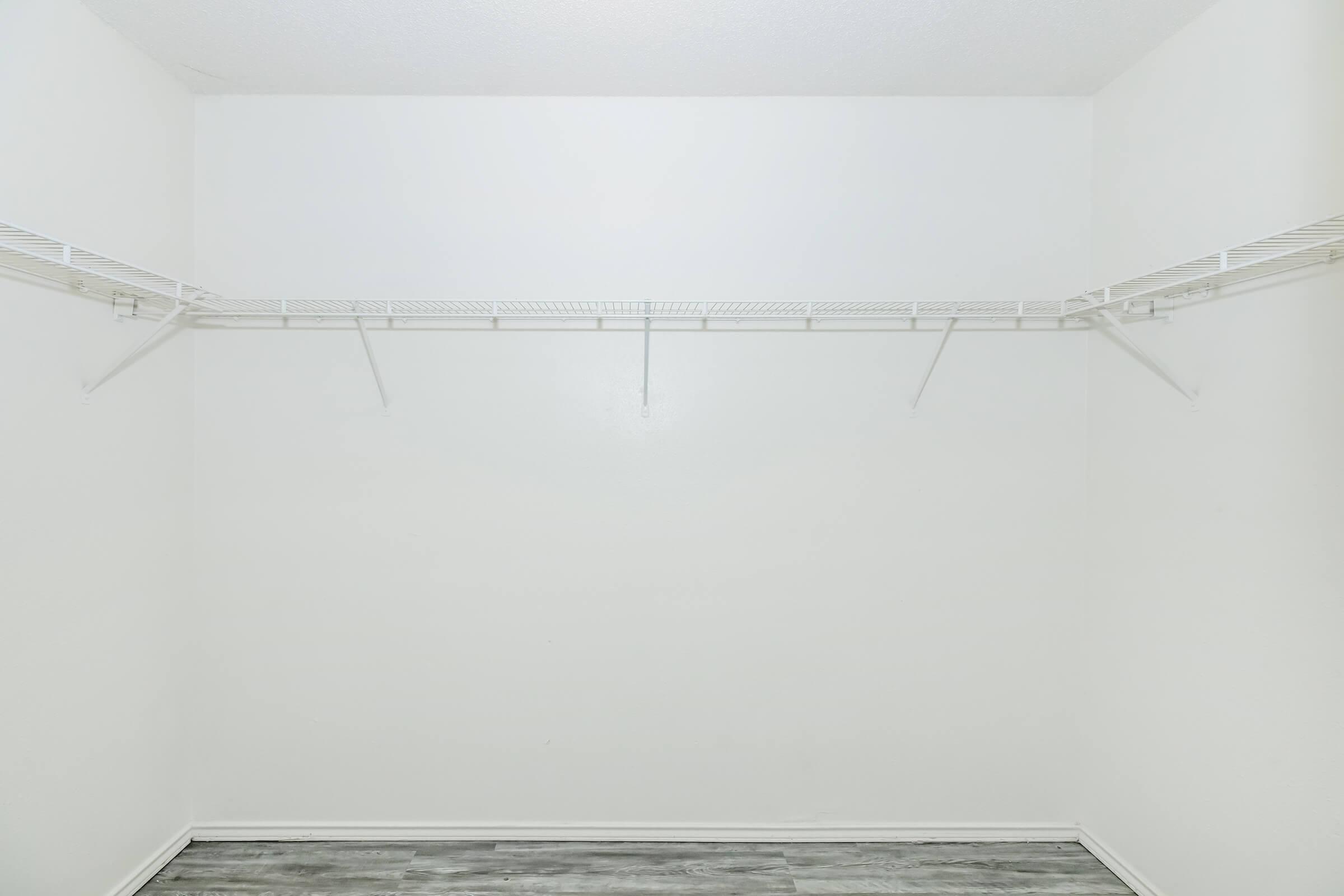Empty closet with white walls and a light gray floor. Two wire shelving units are mounted on opposite walls, providing storage space. The overall atmosphere is clean and minimalistic, with no items or furniture in the closet.