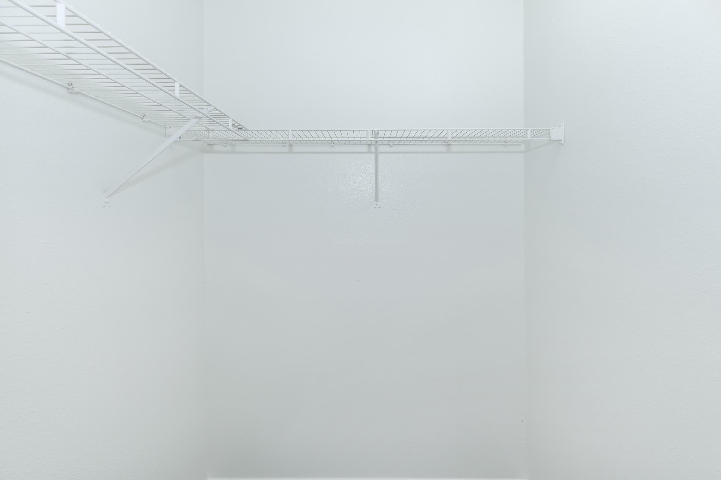 Empty closet with plain white walls and a metal wire shelving unit on one side. The space is uncluttered and minimalistic, emphasizing the lack of items stored within.