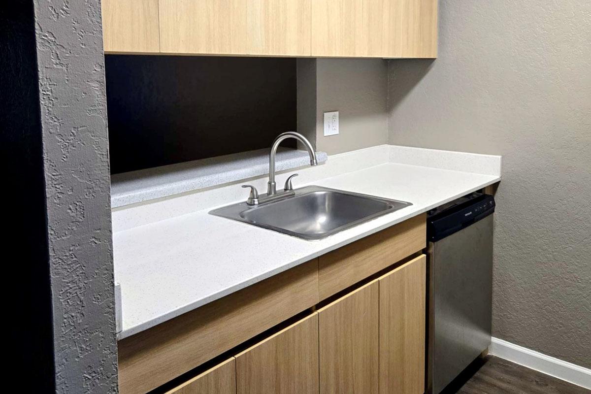 Modern kitchen with wooden cabinets, a stainless steel sink, and gray walls. It features a countertop, a dishwasher, and a minimalist design, showcasing a clean and functional layout.