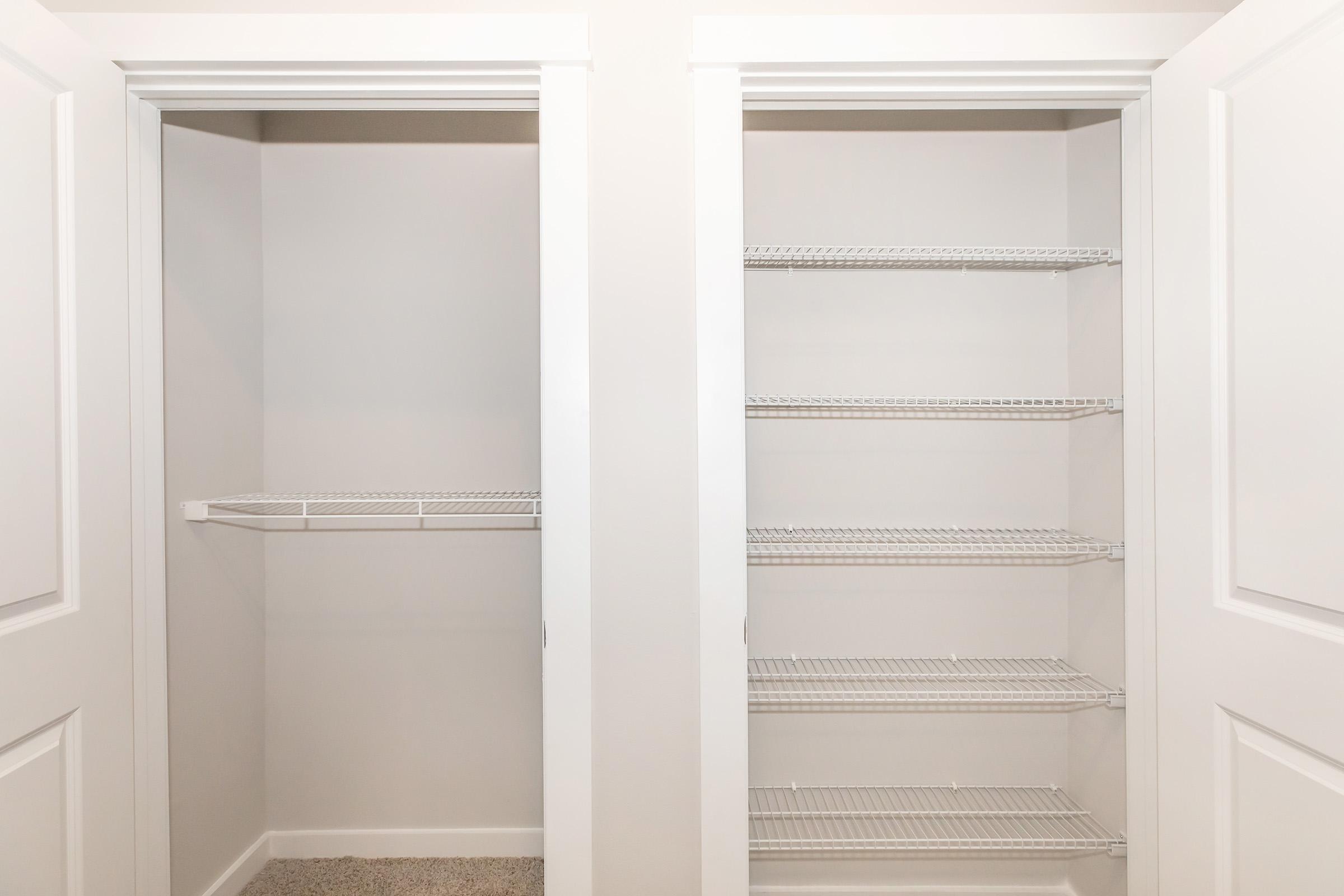 A well-organized closet with two sections: the left side features a single shelf, while the right side has multiple wire shelves, all set against light-colored walls and carpeted flooring. The doors are white, adding a clean and modern look to the space.