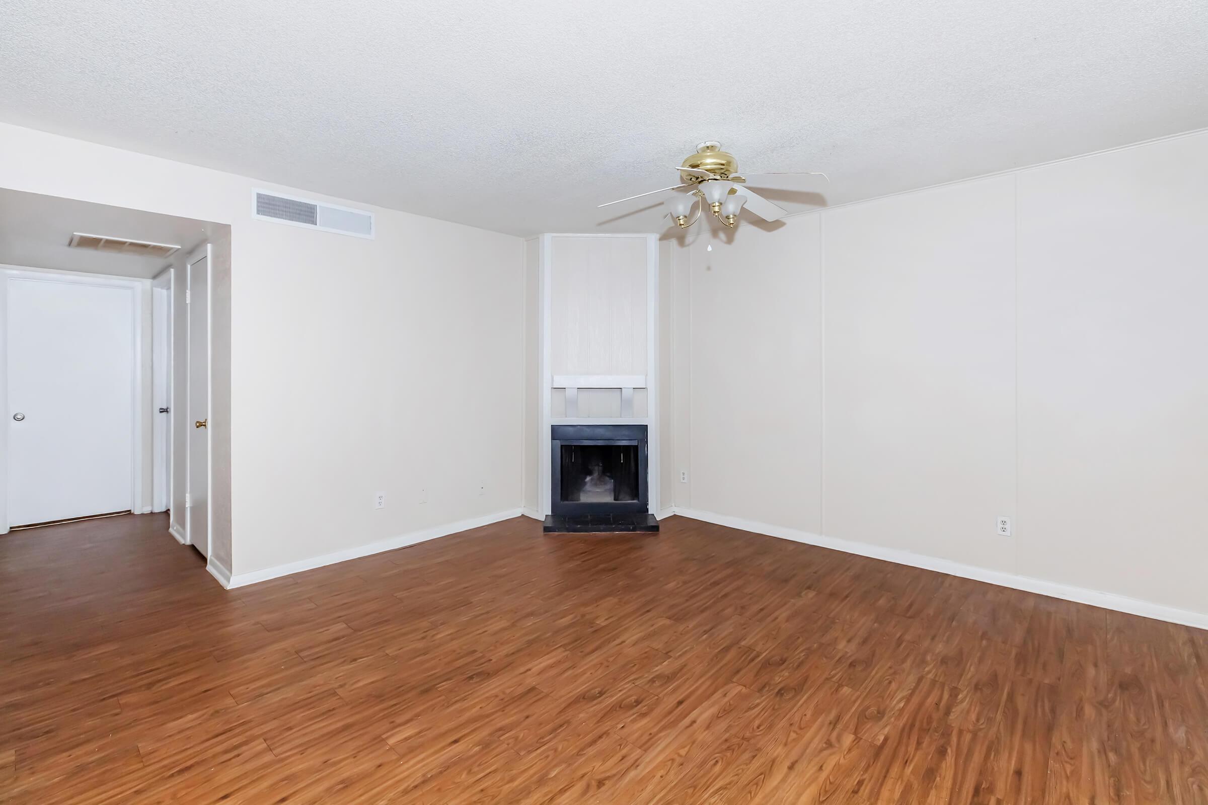 Empty room featuring a hardwood floor, painted beige walls, and a ceiling fan. A fireplace is located on one wall, and there are two doorways leading to adjacent rooms. The space is well-lit and offers a blank canvas for decoration.