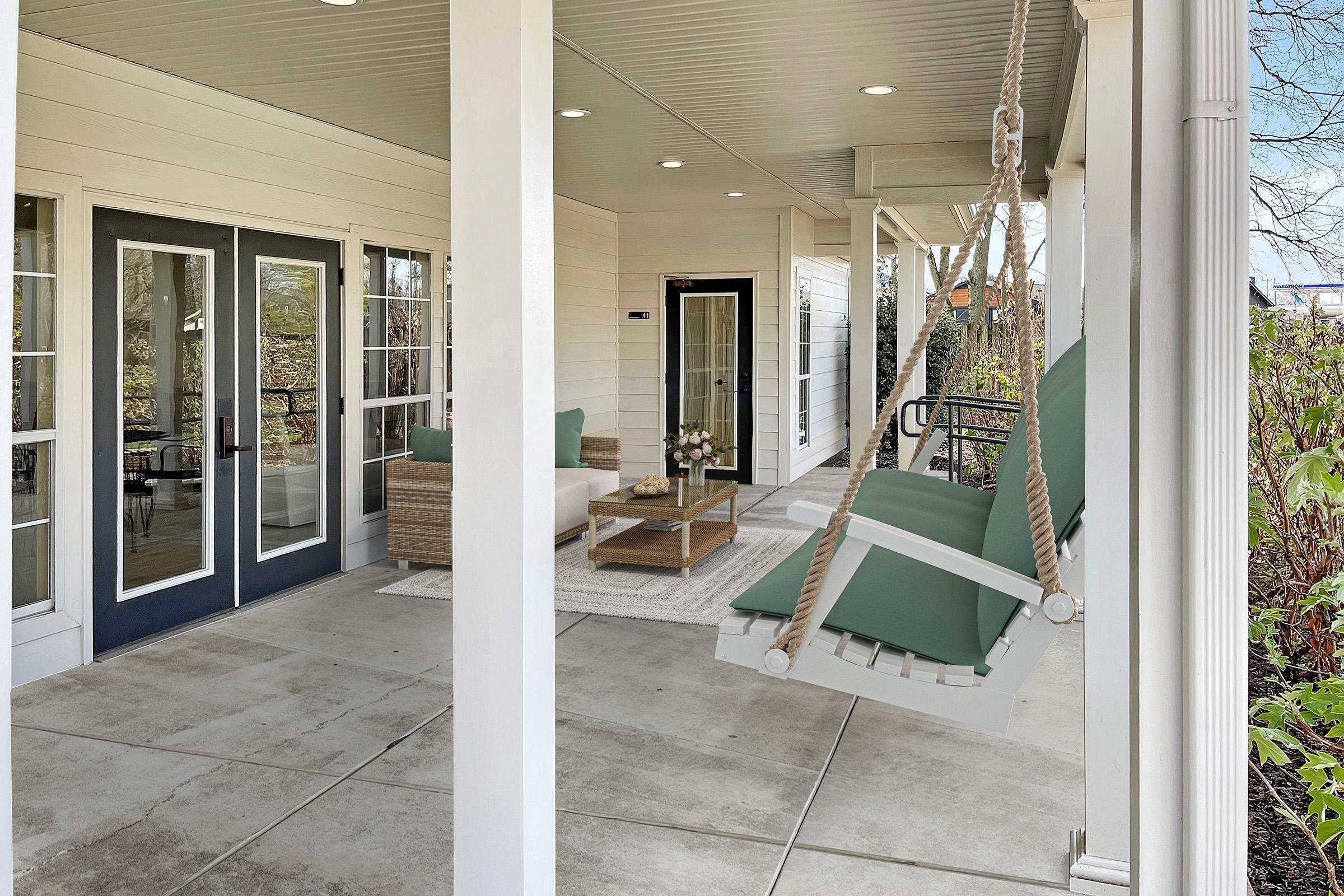 A cozy porch featuring a swing chair with green cushions, a small coffee table on a light rug, and a seating area with wicker furniture. Brightly lit with large windows and doors, the space is surrounded by greenery, creating a welcoming outdoor retreat in Lebanon, TN.
