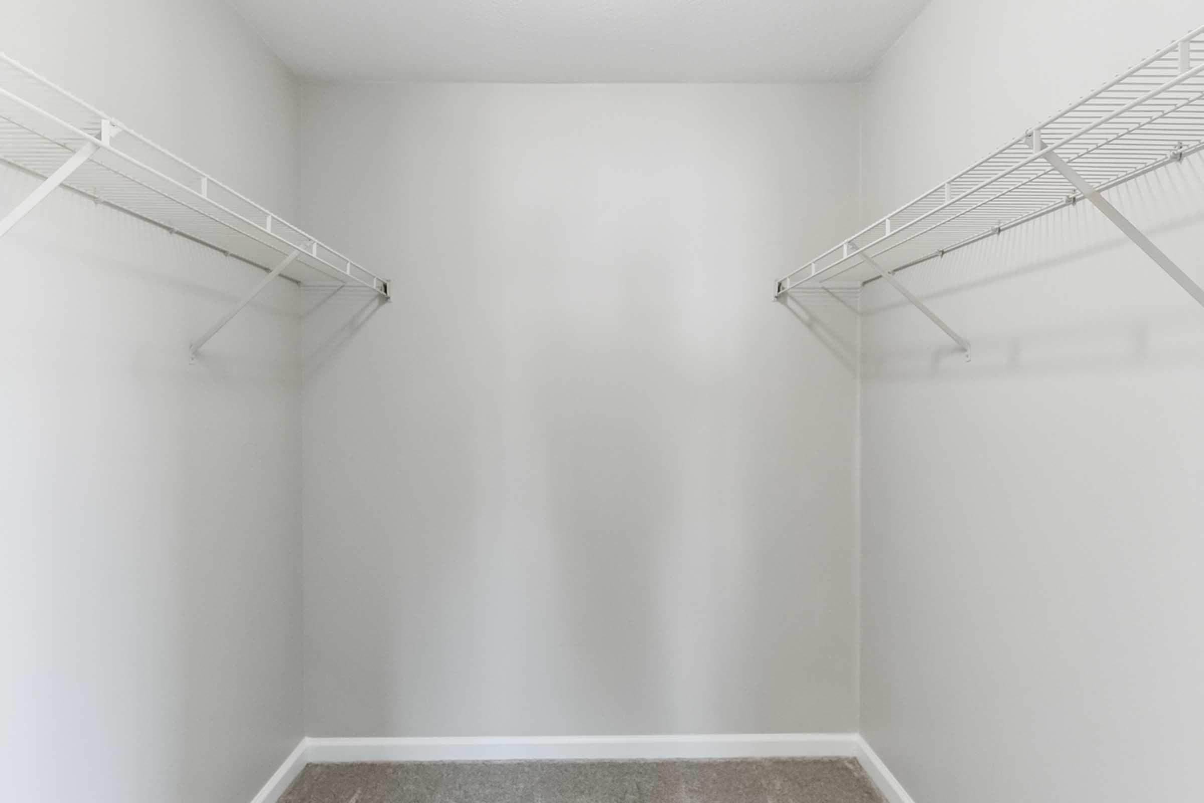 Empty closet space with two wire shelving units mounted on the walls. The walls are painted a light color, and the floor is carpeted in a neutral shade, creating a clean and minimalistic look.