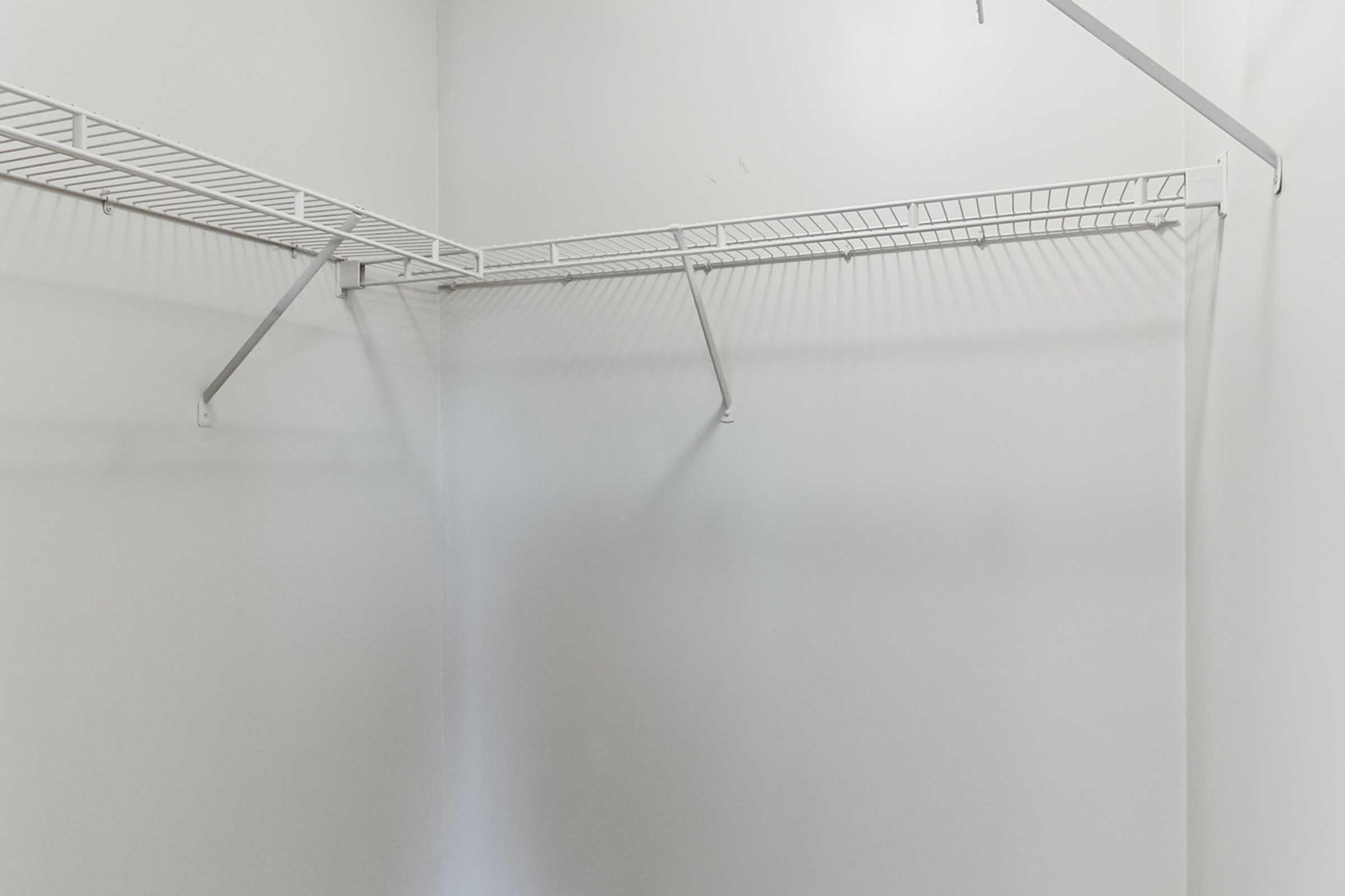 A minimalistic, empty closet featuring white wire shelves and walls. The shelves are positioned on the upper part of the closet, casting subtle shadows, emphasizing the space's uncluttered and open appearance.