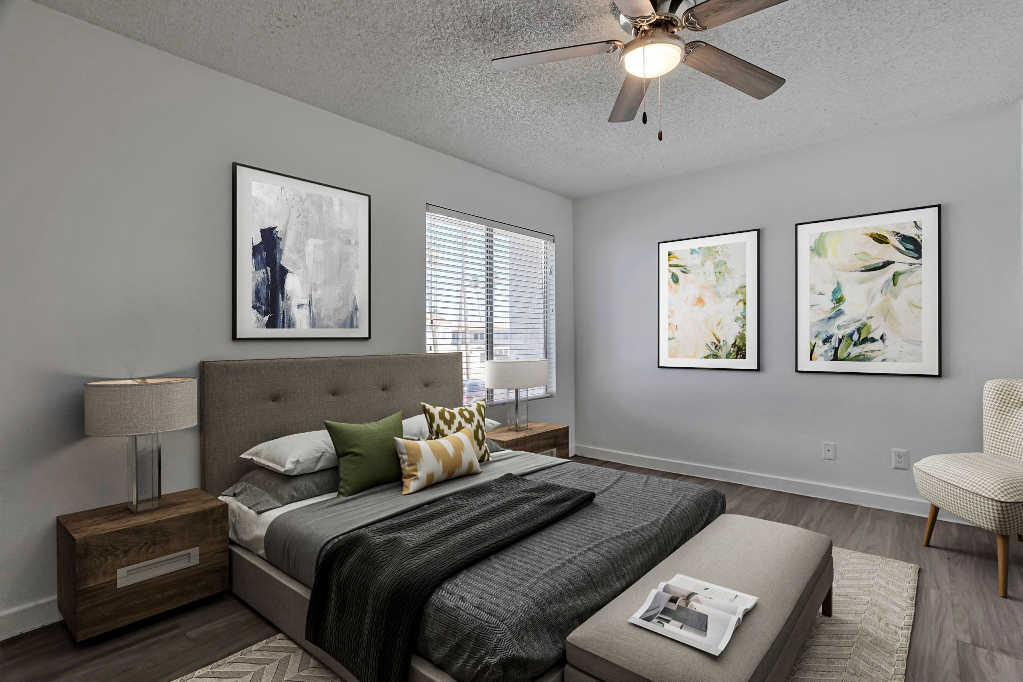 A modern bedroom featuring a gray upholstered bed with decorative pillows, two wooden bedside tables with lamps, and a light gray armchair. The walls are adorned with three framed artworks. Natural light streams through a window with blinds, creating a warm and inviting atmosphere.