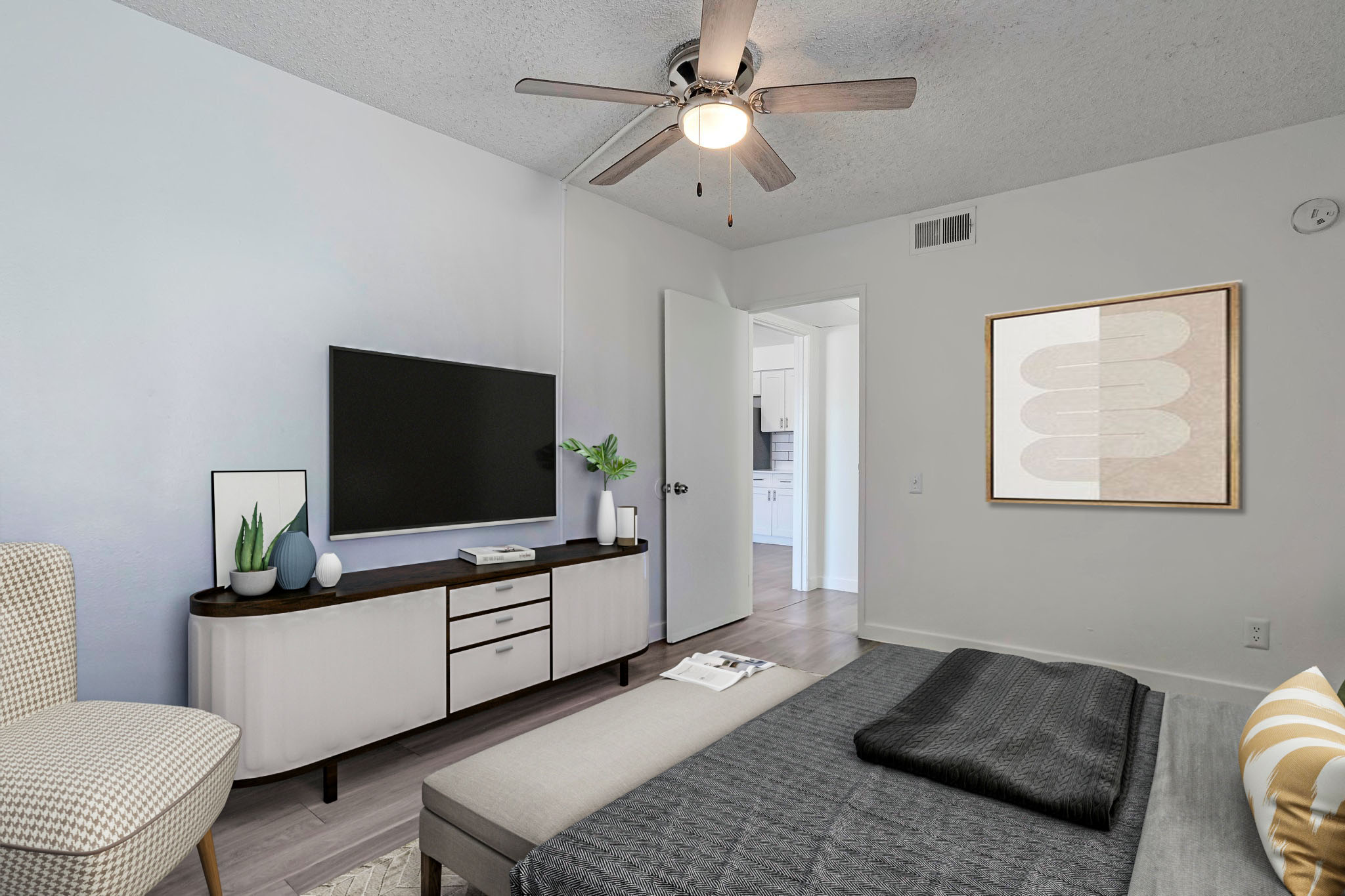 A modern bedroom featuring a light color scheme, a ceiling fan, and a neatly made bed with dark bedding. There's a sleek entertainment unit with a flat-screen TV, decorative plants, and an abstract art piece on the wall. A cozy chair is positioned nearby, adding to the inviting atmosphere.